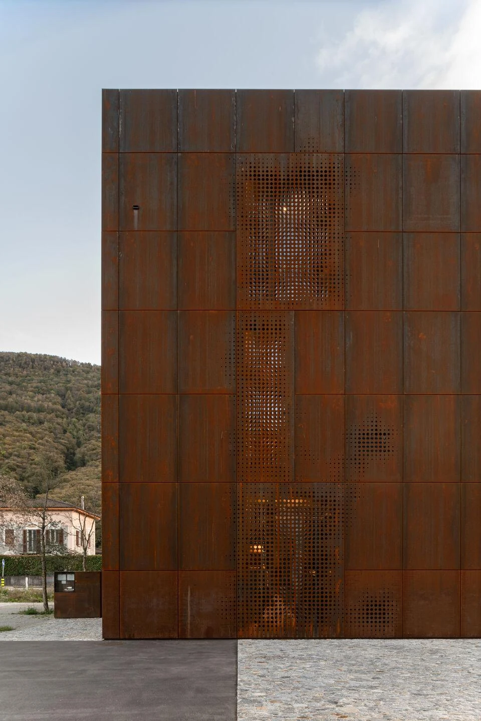 Urs Hauser Winery by WDMRA, photographed by Giacomo Albo — A corner of the cube with a vertical perforated band, cobblestone paving and gravel meeting at its foot.