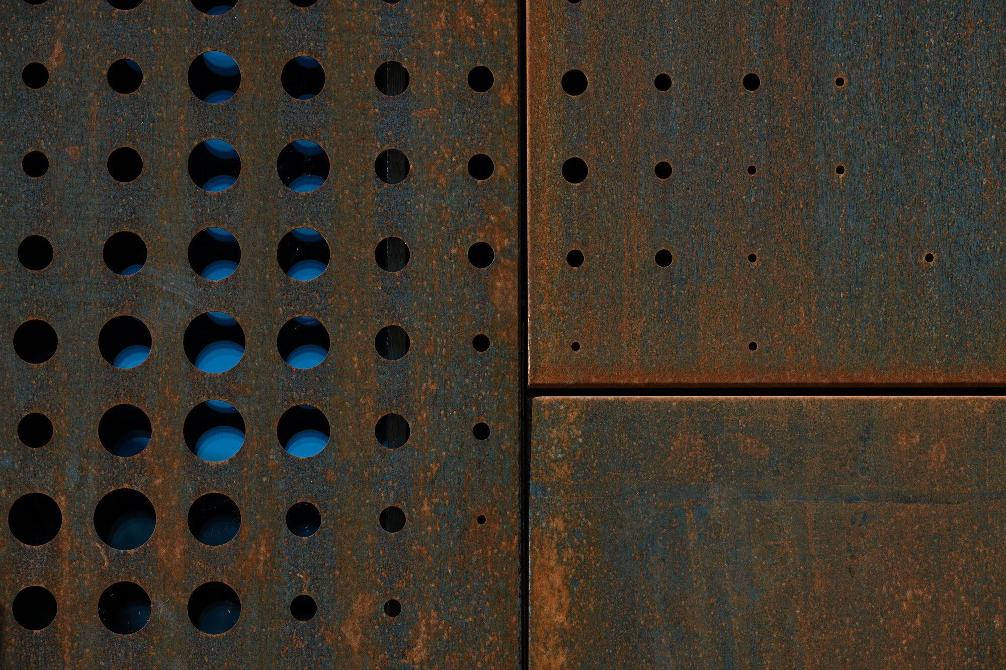 Urs Hauser Winery by WDMRA, photographed by Giacomo Albo — A macro of the perforation, blue sky showing through round holes punched into rusted steel.