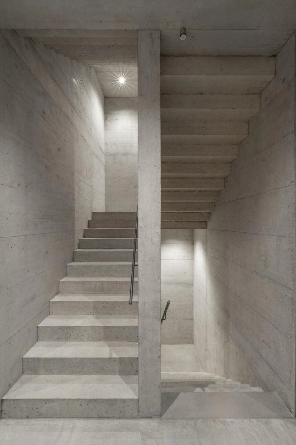 Urs Hauser Winery by WDMRA, photographed by Giacomo Albo — A cast-concrete stair climbing past a central pier under a small overhead light.