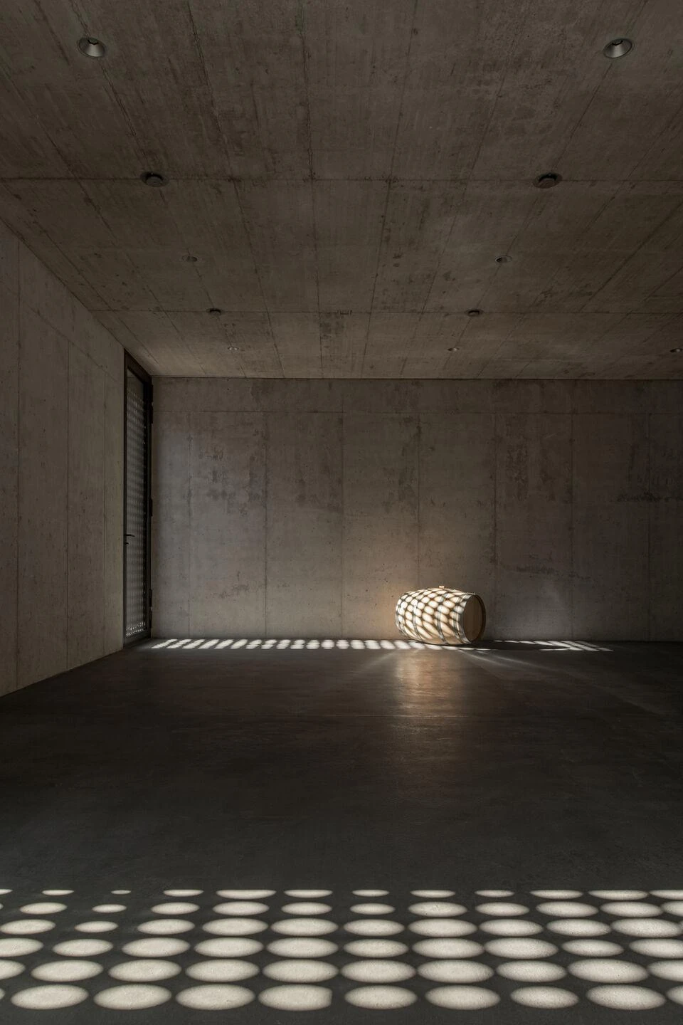 Urs Hauser Winery by WDMRA, photographed by Giacomo Albo — A near-empty concrete room, a single barrel lit by a broad field of dots cast from a perforated screen.
