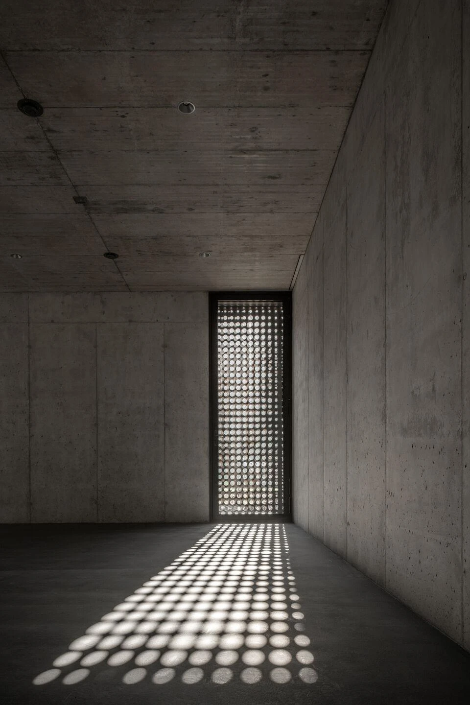 Urs Hauser Winery by WDMRA, photographed by Giacomo Albo — A concrete interior where a tall perforated slot casts a long carpet of light dots across the floor.