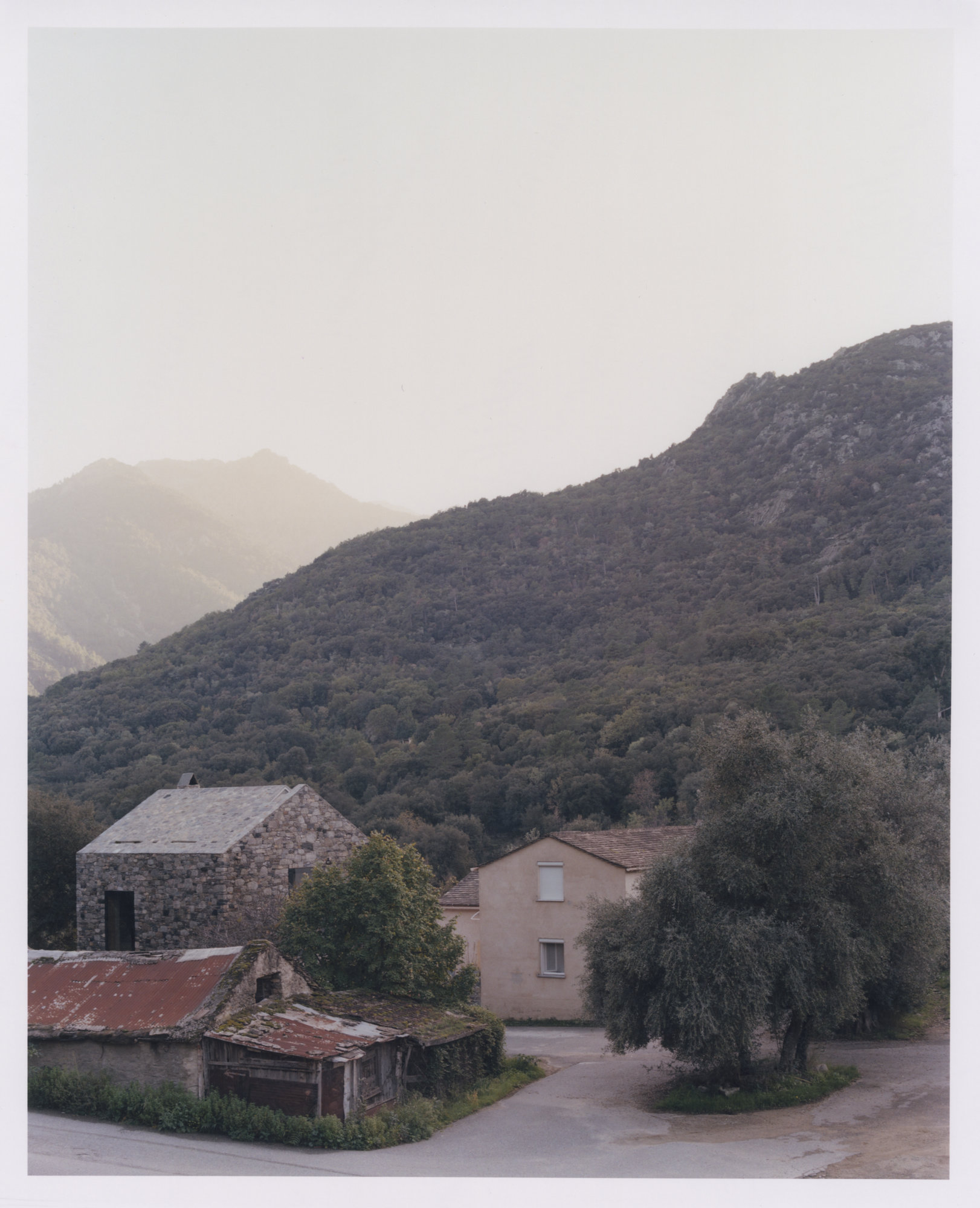 Office Orma Architettura by Orma Architettura — The office and its pitched stone-slab roof seen from above, set among older village roofs with forested mountains behind.