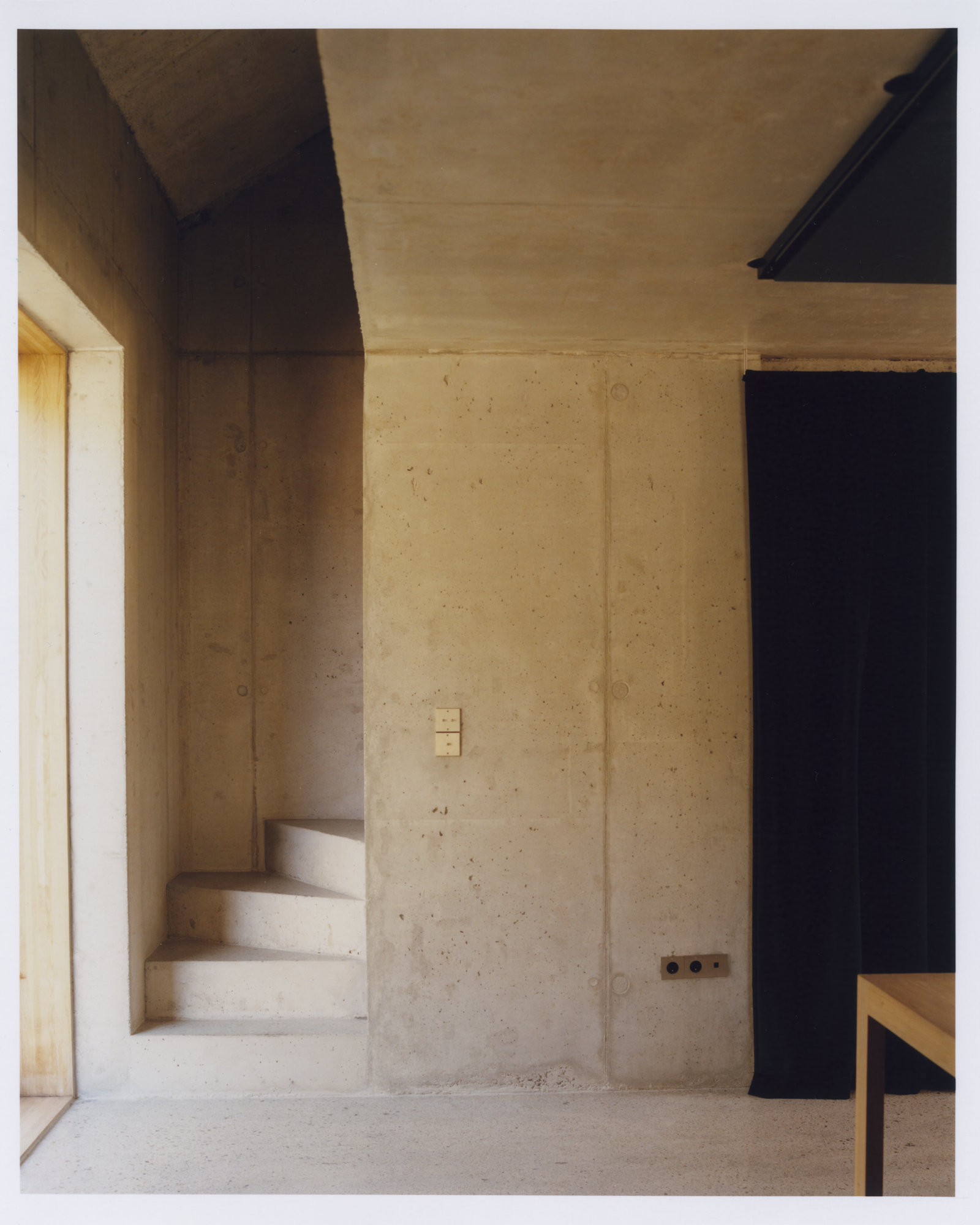 Office Orma Architettura by Orma Architettura — A concrete stair turning against a board-formed concrete wall, a pale timber opening at left and a dark curtain at right.