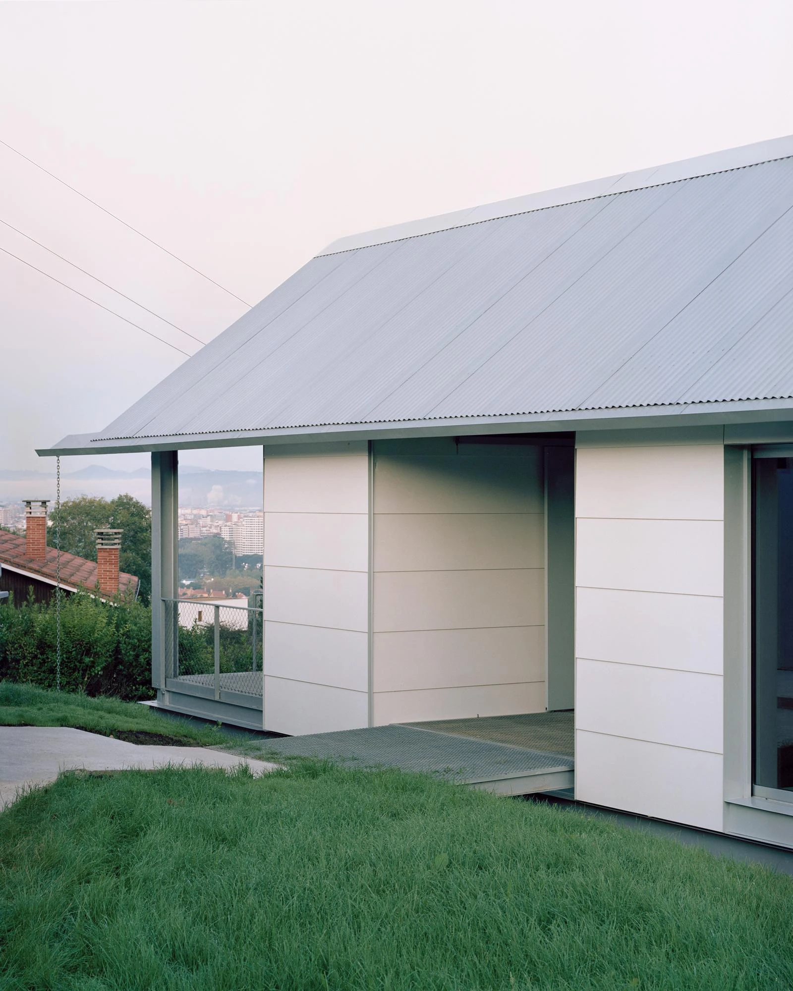 Casa Guadalupe by HANGHAR, photographed by Rory Gardiner — A corner where white sandwich panels slide back beneath the corrugated eave to open onto a galvanized-grating porch.