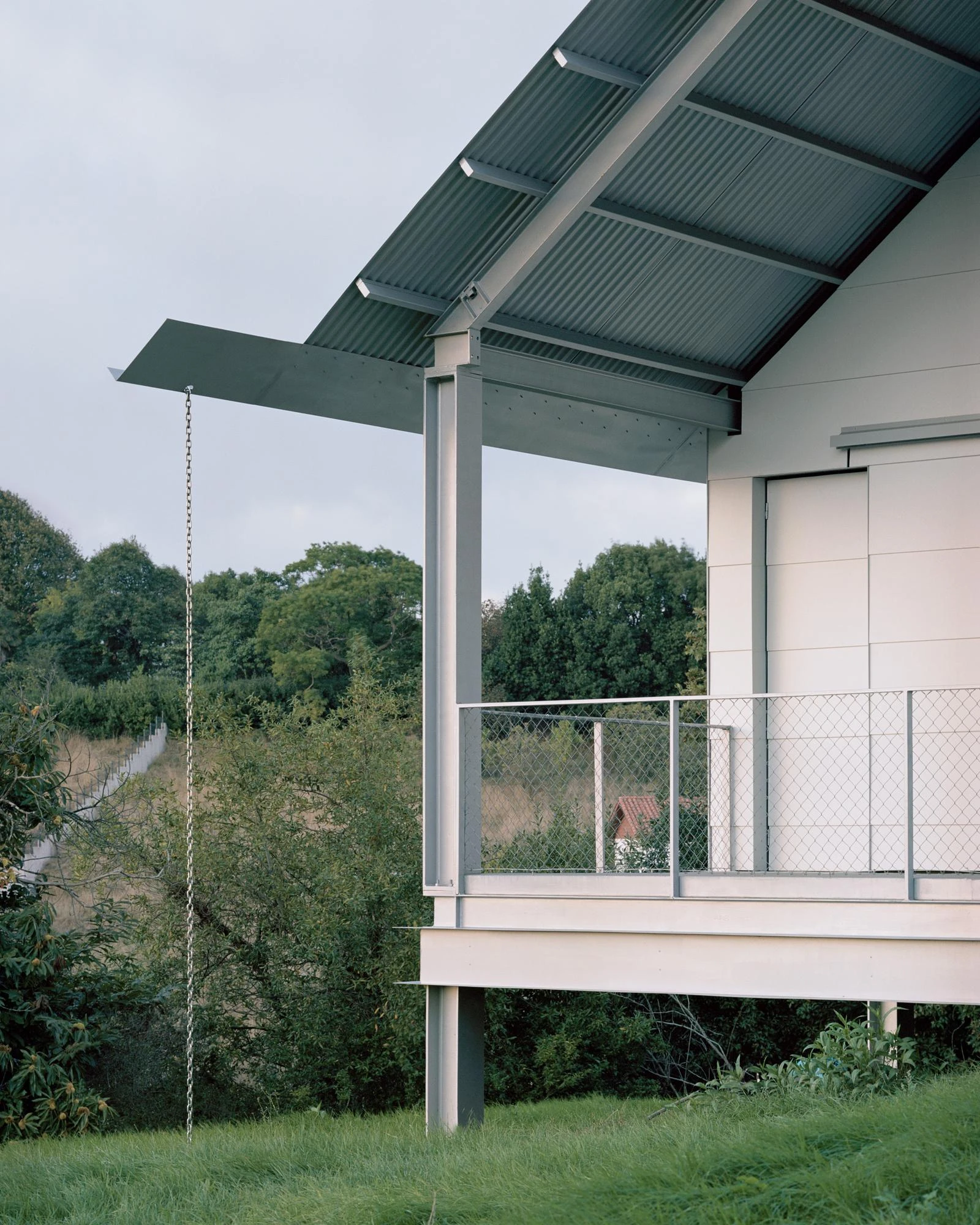 Casa Guadalupe by HANGHAR, photographed by Rory Gardiner — A corner of the eave and steel structure with the downpipe chain, set against dark trees.