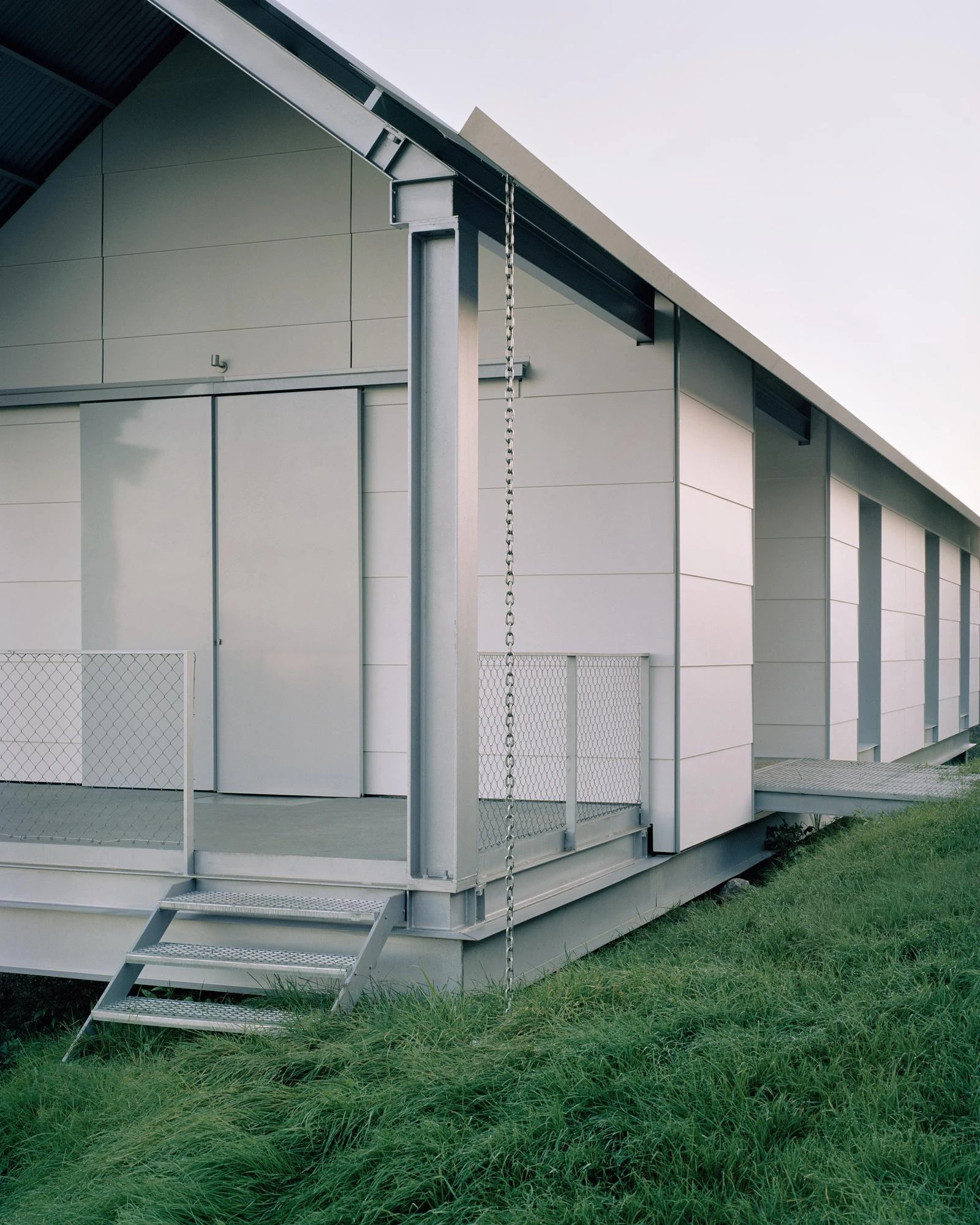 Casa Guadalupe by HANGHAR, photographed by Rory Gardiner — The long side elevation, its grey steel plinth and sliding panels running above a galvanized walkway.