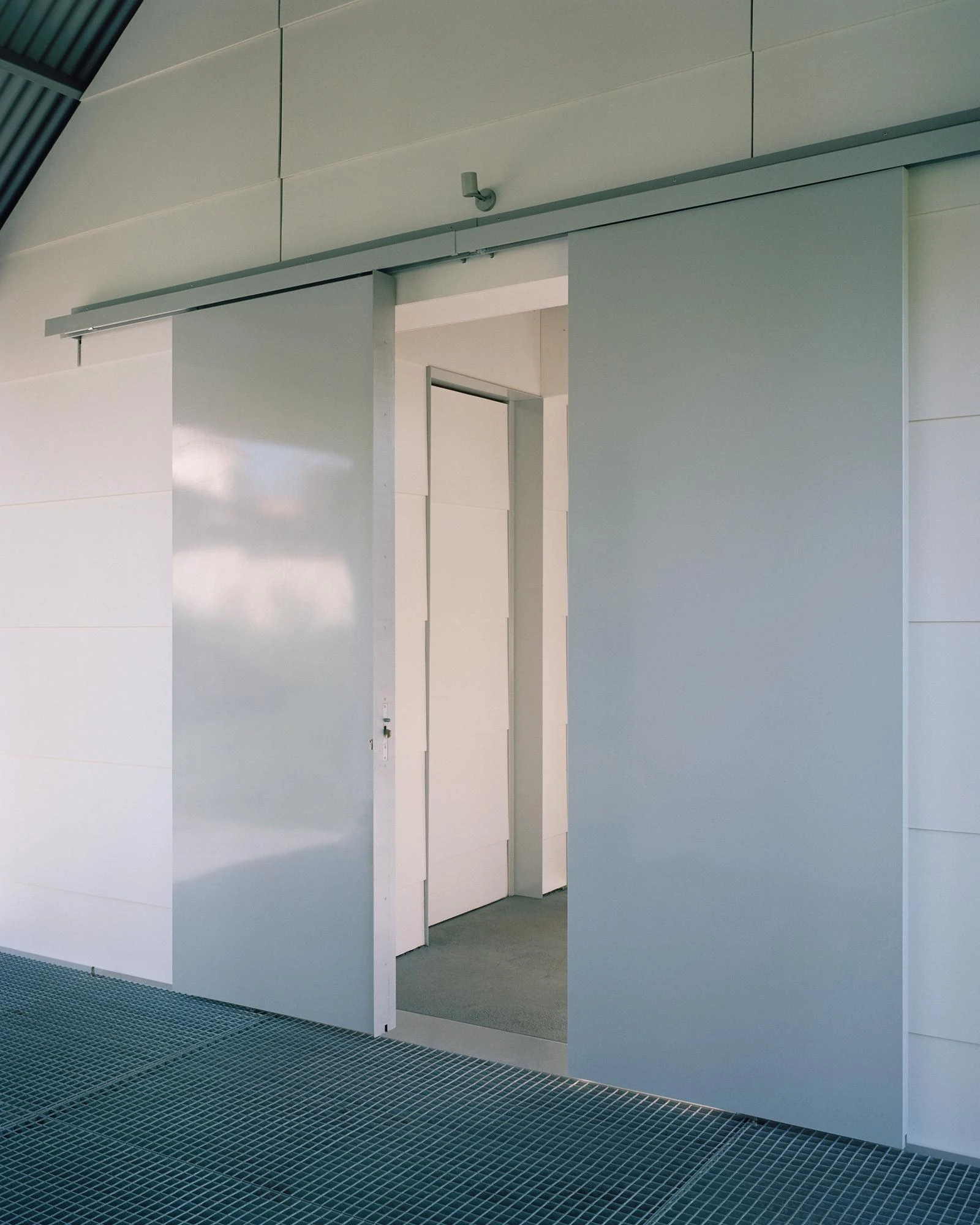 Casa Guadalupe by HANGHAR, photographed by Rory Gardiner — A porch detail where a grey sliding panel draws back to reveal a white interior door.