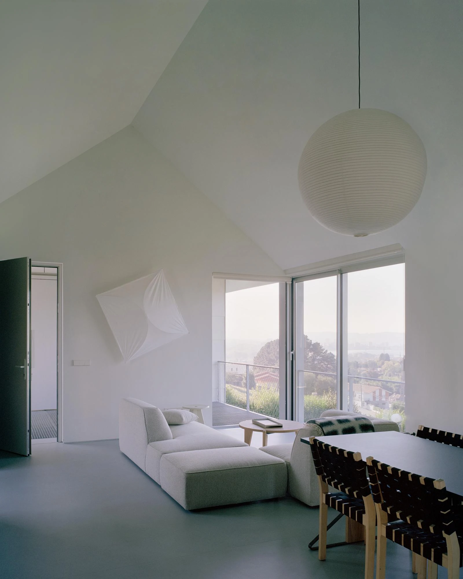 Casa Guadalupe by HANGHAR, photographed by Rory Gardiner — The living room under a white pitched ceiling, a Noguchi Akari lantern hung above a white modular sofa.