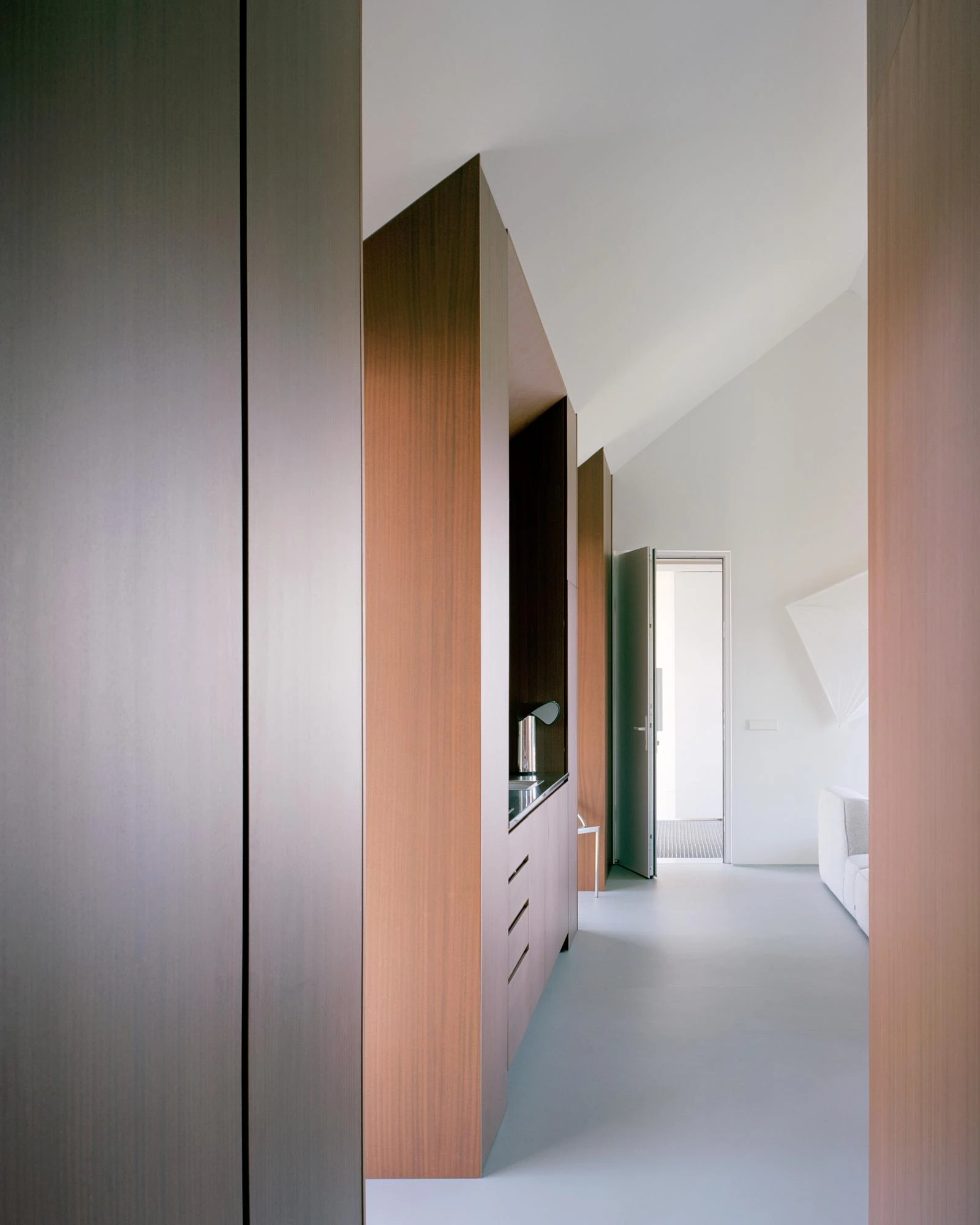 Casa Guadalupe by HANGHAR, photographed by Rory Gardiner — A corridor lined with sapele volumes over a pale blue-grey resin floor.