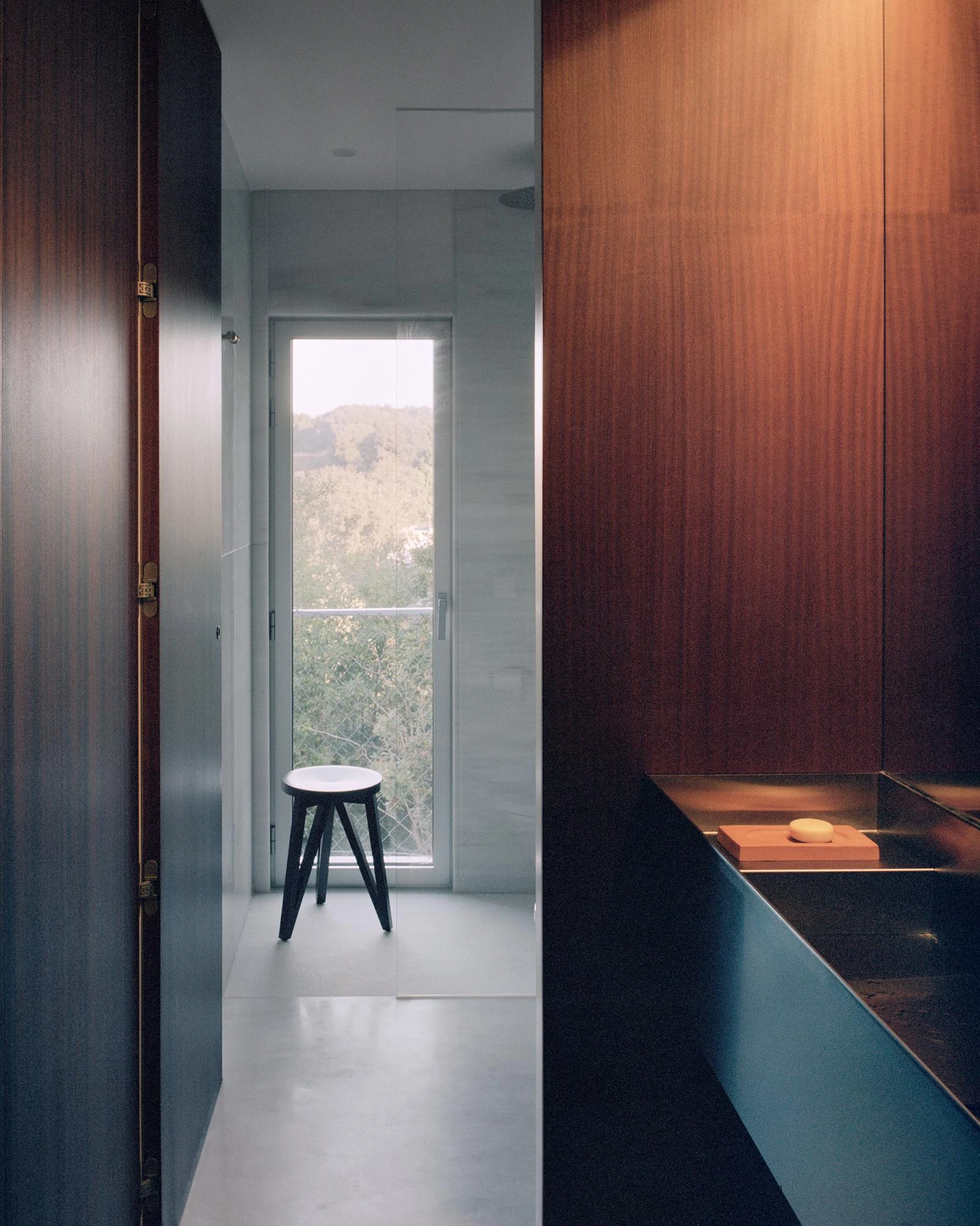 Casa Guadalupe by HANGHAR, photographed by Rory Gardiner — A bathroom clad in sapele with a stainless trough basin and a glass shower.