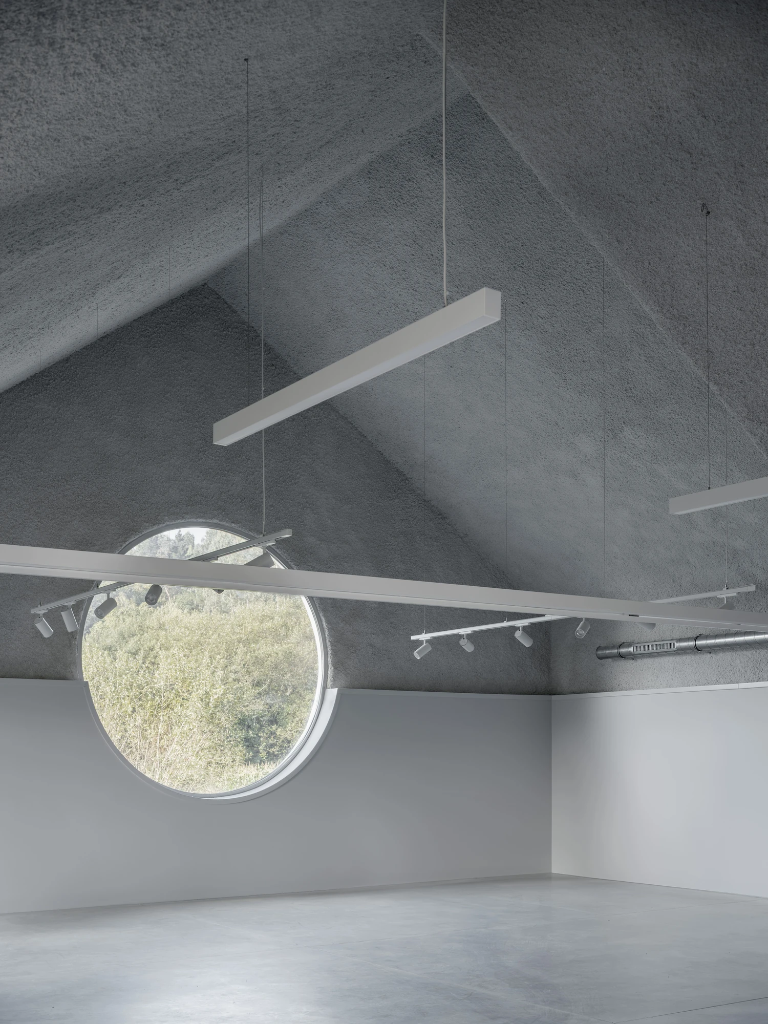 Goians Community Center by NULA.STUDIO + FCA, photographed by Luis Díaz Díaz / NULA.STUDIO — A round oculus framing green trees sits below the folded rockwool ceiling, a suspended linear light crossing the room.
