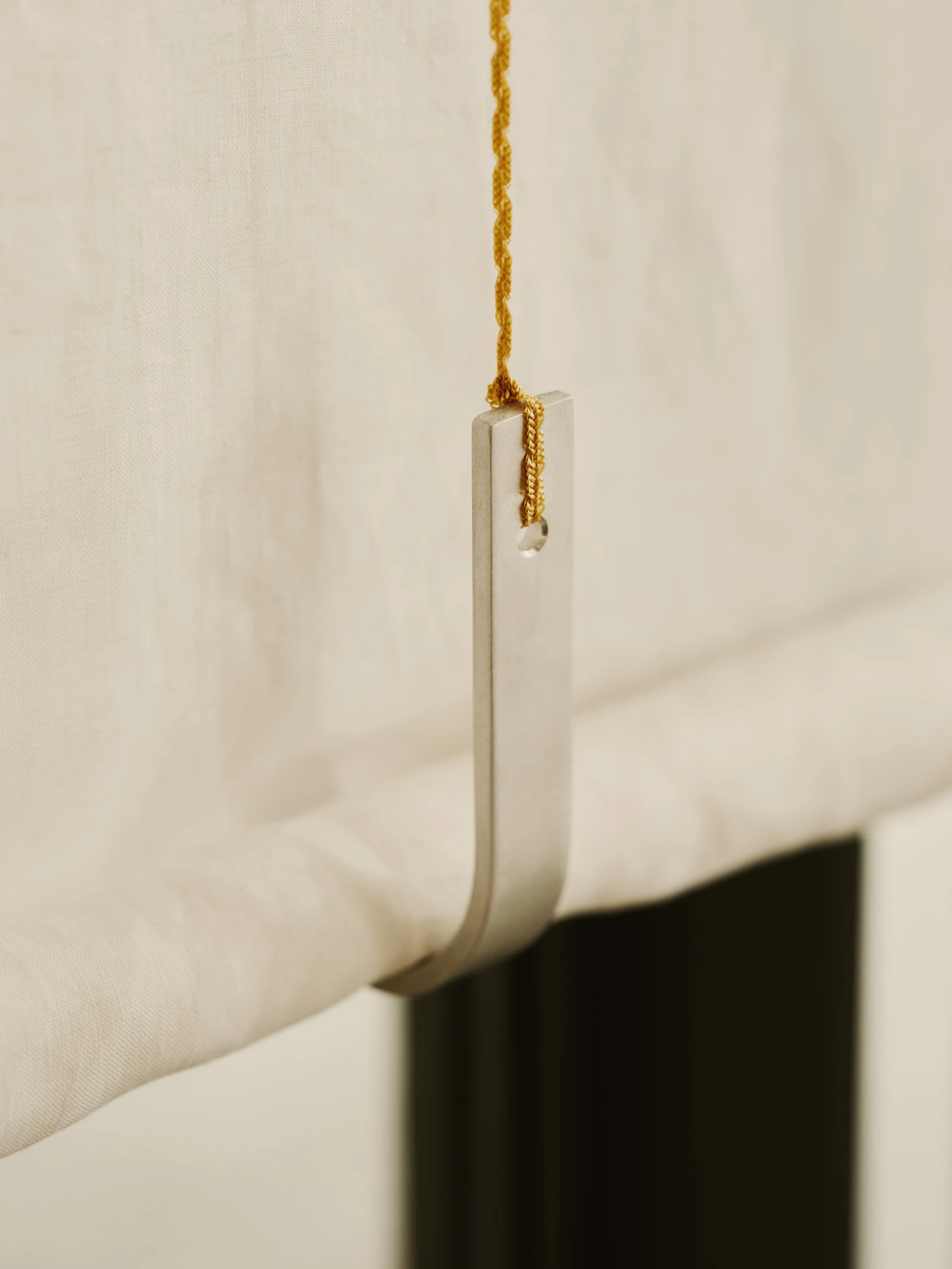 Nichigetsu by Studio Inhalt_, photographed by Robert Rieger — A close view of a linen curtain weighted by a slim metal bar on a twisted gold cord, the fabric falling in soft folds.