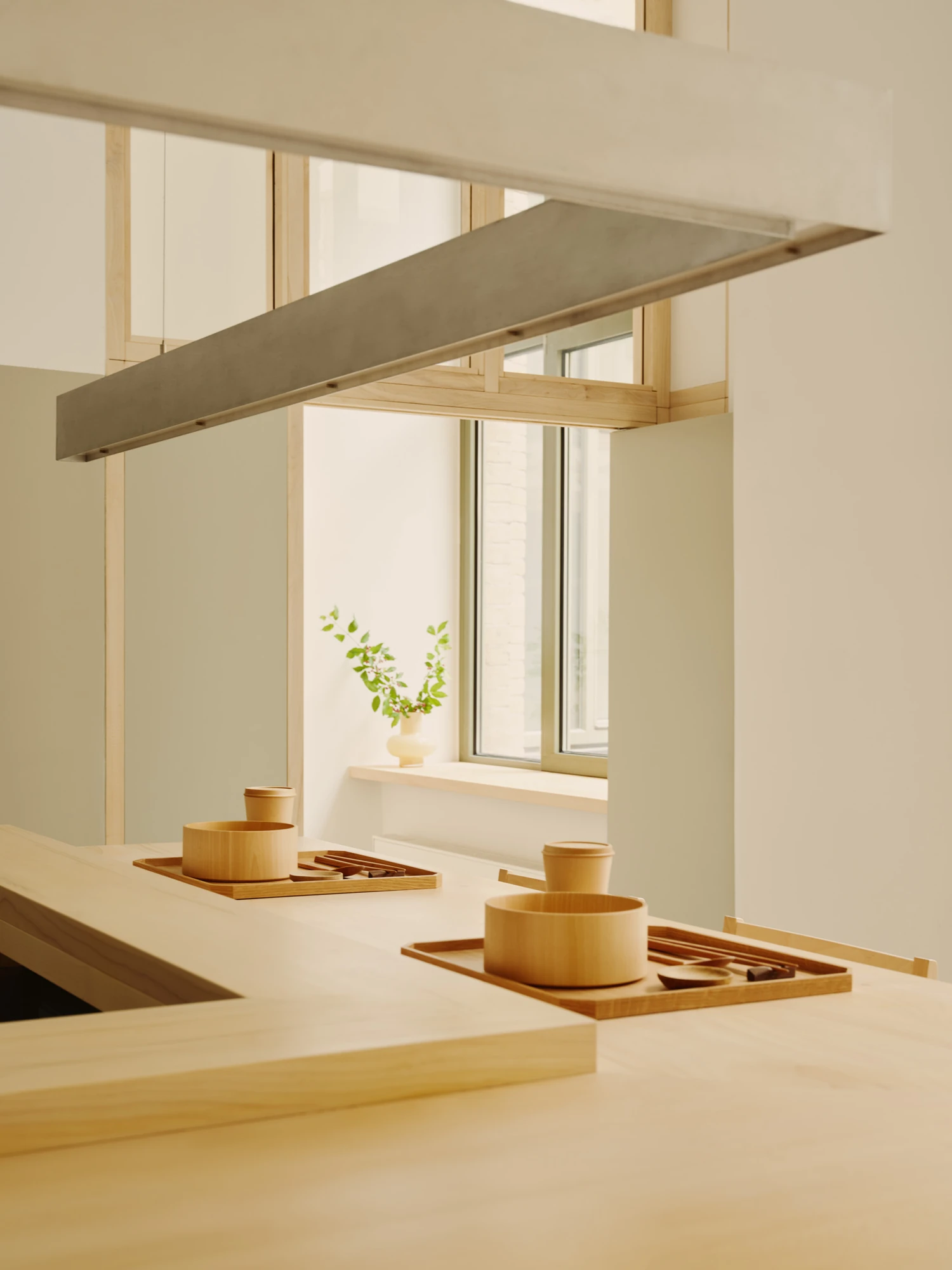 Nichigetsu by Studio Inhalt_, photographed by Robert Rieger — Wooden trays of turned bowls and cups line the maple counter beneath a steel pendant, a window nook holding a single branch beyond.