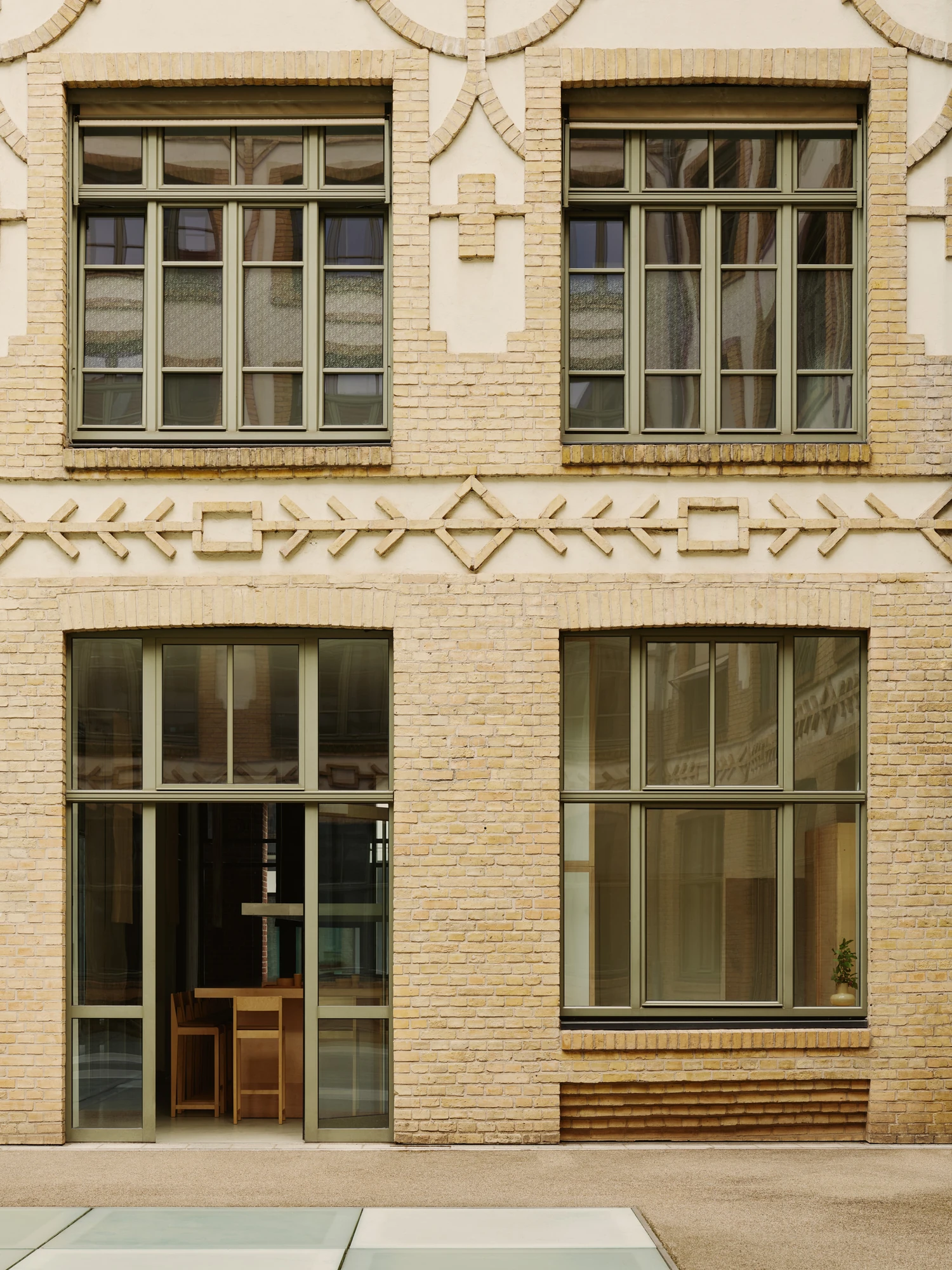 Nichigetsu by Studio Inhalt_, photographed by Robert Rieger — The ornamental yellow-brick facade with its Jugendstil patterning and olive-green window frames, a glimpse of the maple counter through the door.