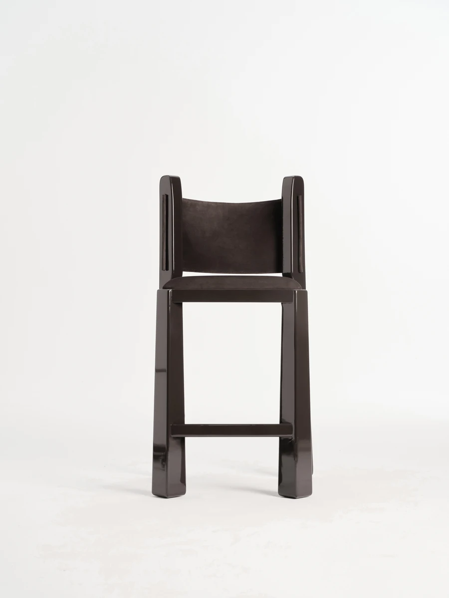 Ruby by NOVSEP, photographed by NOVSEP — A single espresso-lacquered Ruby stool stands front-on against a seamless white ground, its suede sling back suspended between tall gloss uprights.