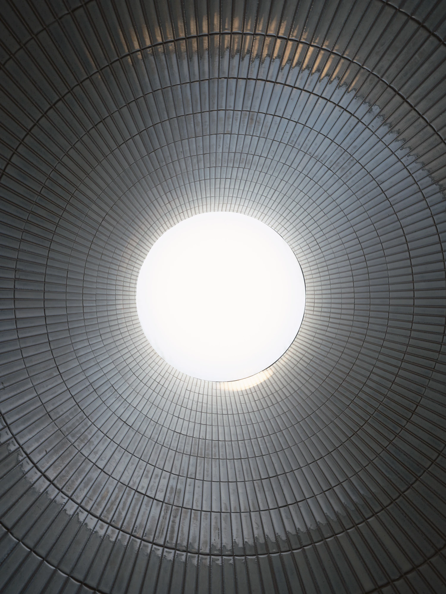 Villa P by Daniel Berg Arkitekter, photographed by Markus Linderoth — Looking straight up the tiled cylinder of a light shaft, concentric courses of pale tile draw the eye to a bright circular sky opening.