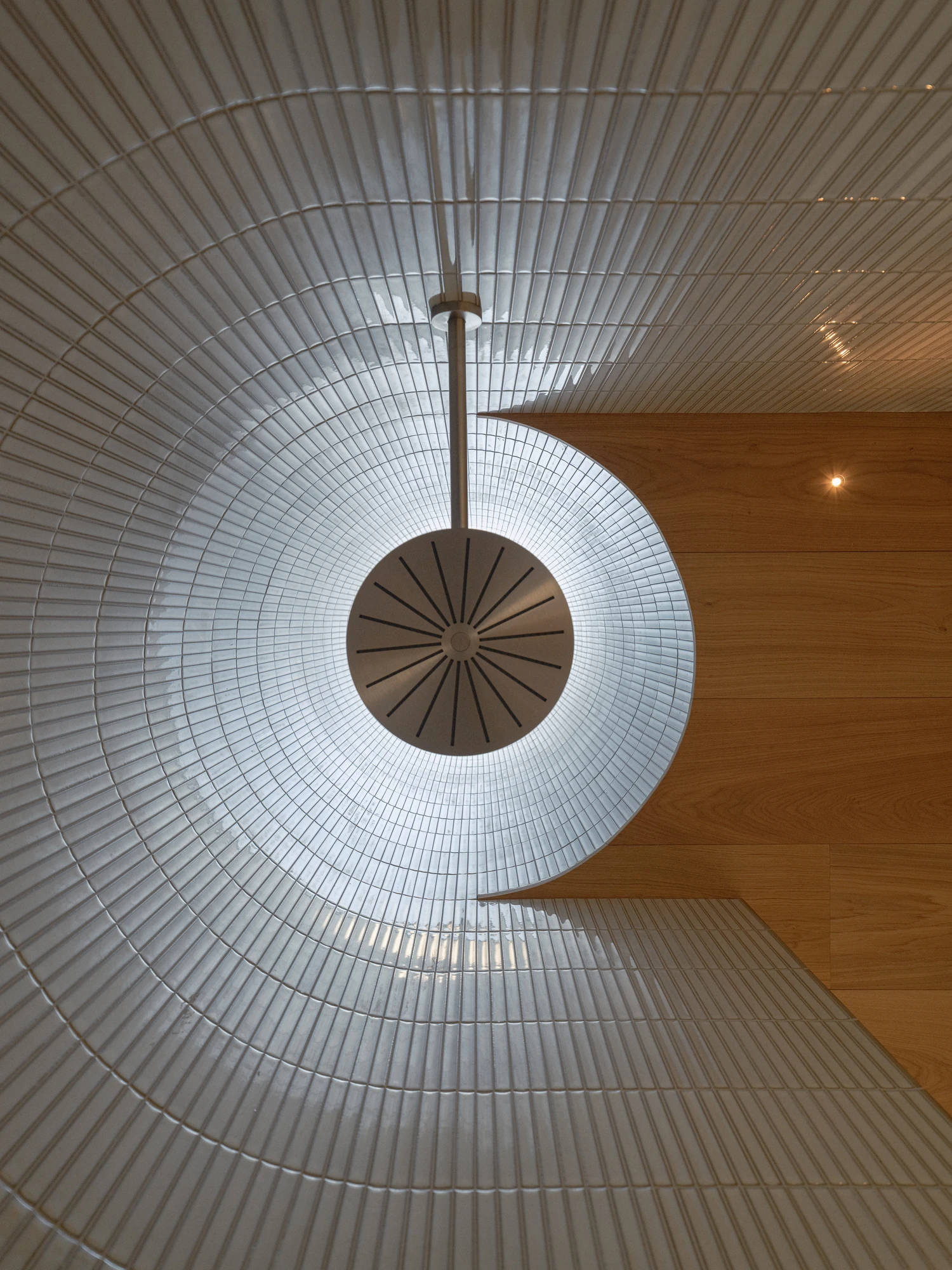 Villa P by Daniel Berg Arkitekter, photographed by Markus Linderoth — A circular rooflight opens at the center of a tiled, funnel-shaped shaft, meeting a flat oak ceiling along one clean edge.
