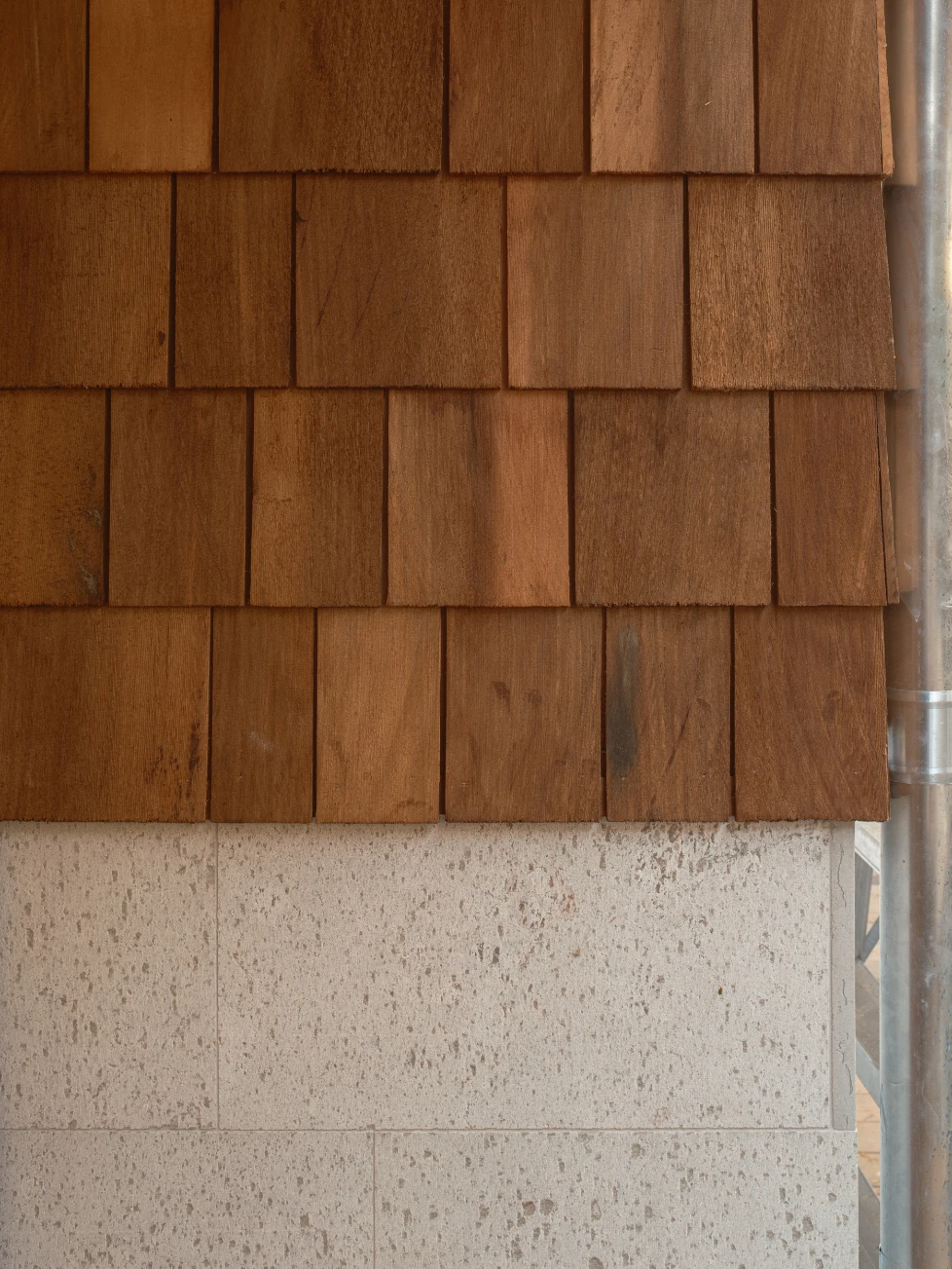 Villa P by Daniel Berg Arkitekter, photographed by Markus Linderoth — Cedar shingles in warm tones meet a base course of pitted grey limestone, a slim metal downpipe running the junction.