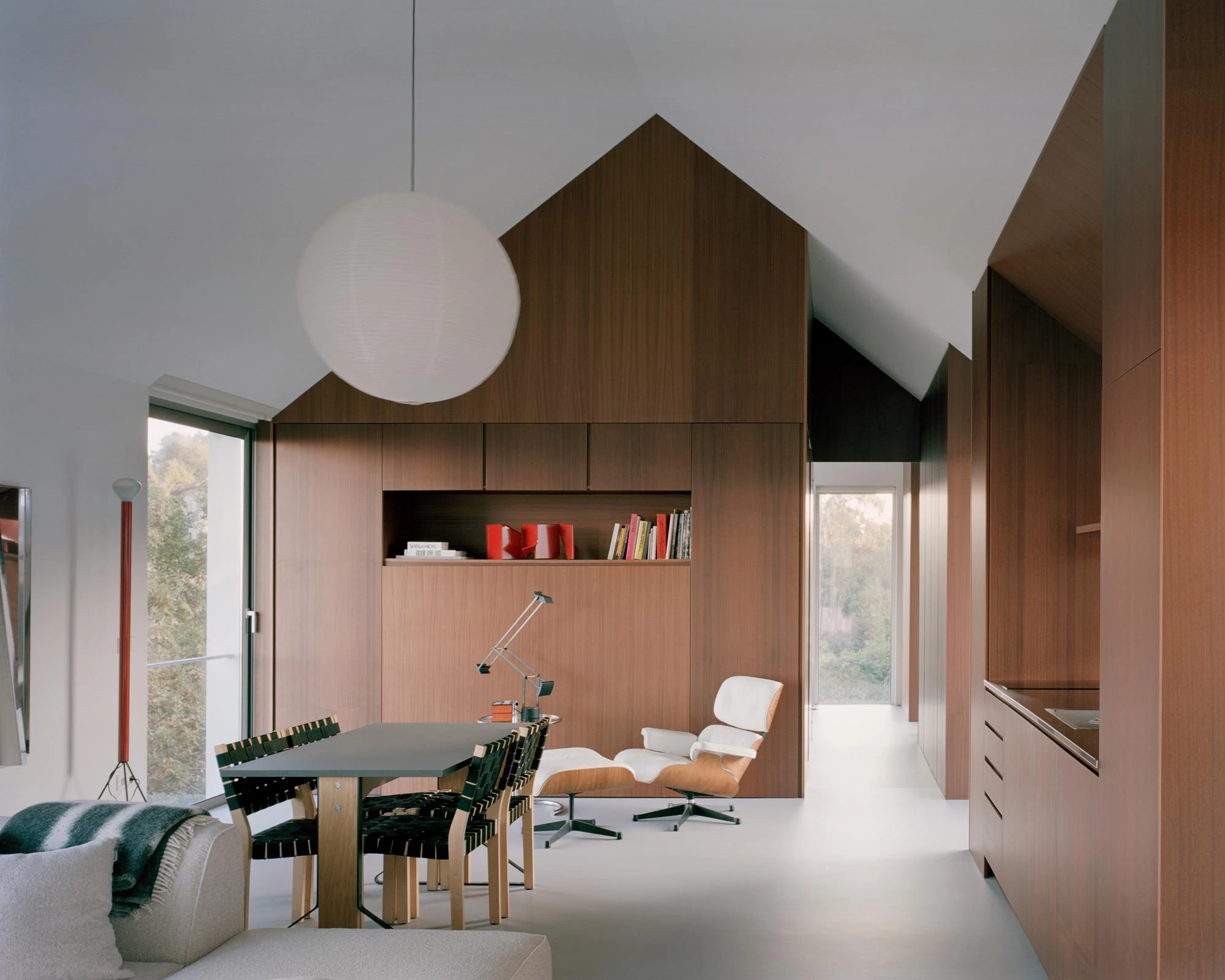 Casa Guadalupe by HANGHAR, photographed by Rory Gardiner — The full width of the wood-lined gable room, the dining table and Aalto chairs at left, the Eames lounge and a doorway to the garden at right.