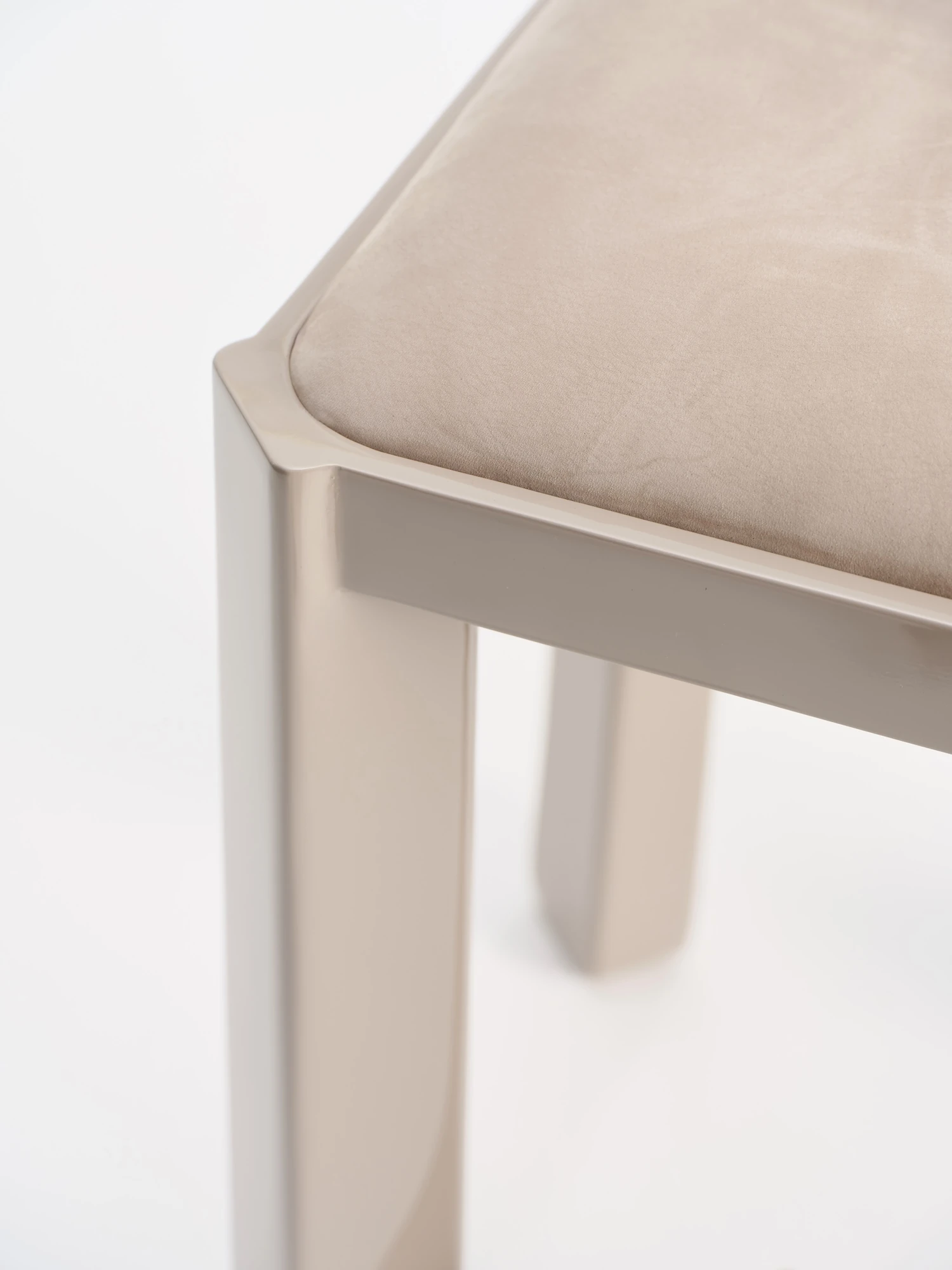 Ruby by NOVSEP, photographed by NOVSEP — Close detail of the greige frame at the seat corner, where the lacquered rail meets two splayed legs beneath the suede cushion.