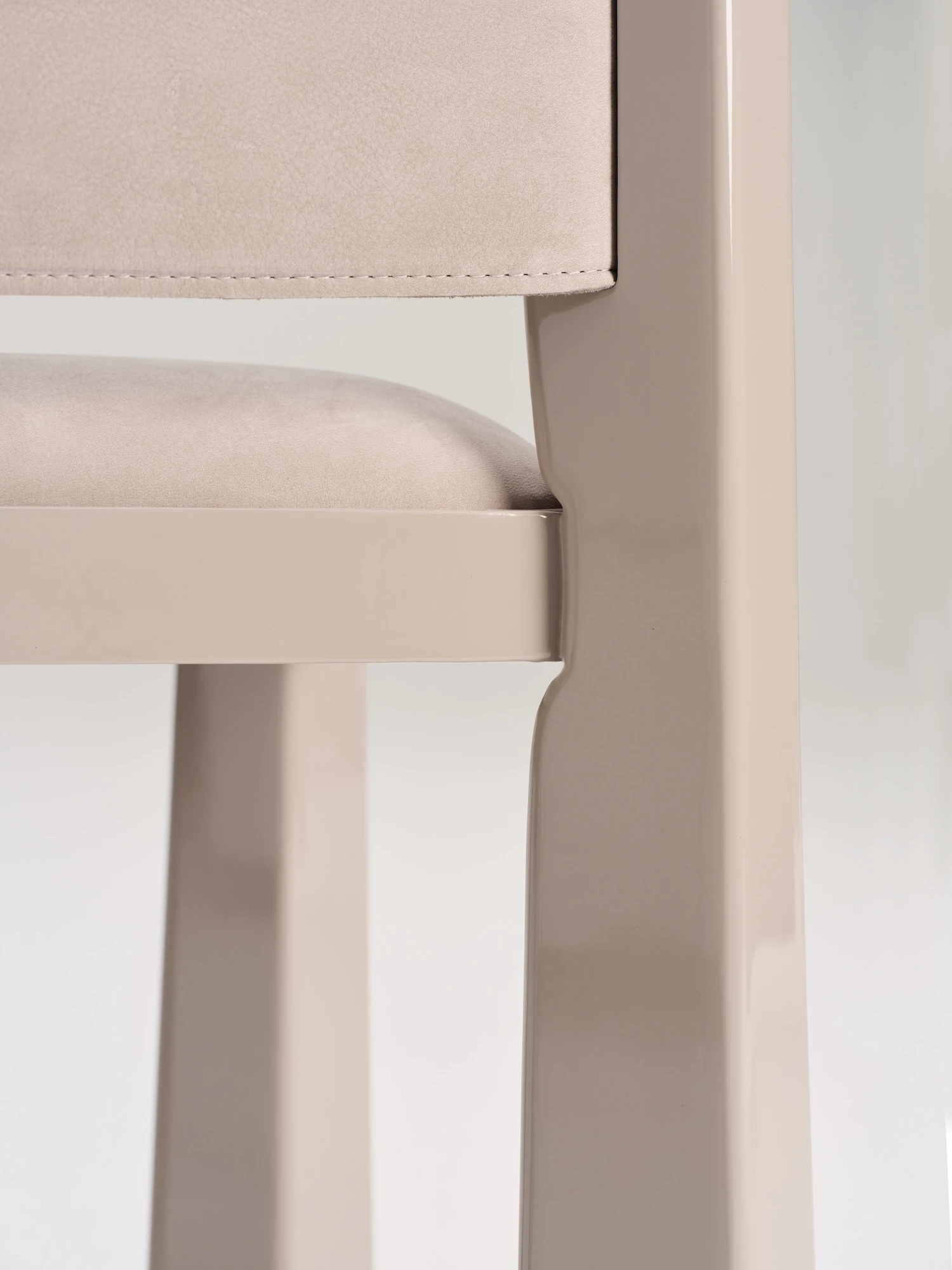 Ruby by NOVSEP, photographed by NOVSEP — Tight crop of the seat edge and a front leg, the stitched suede meeting the gloss lacquer.