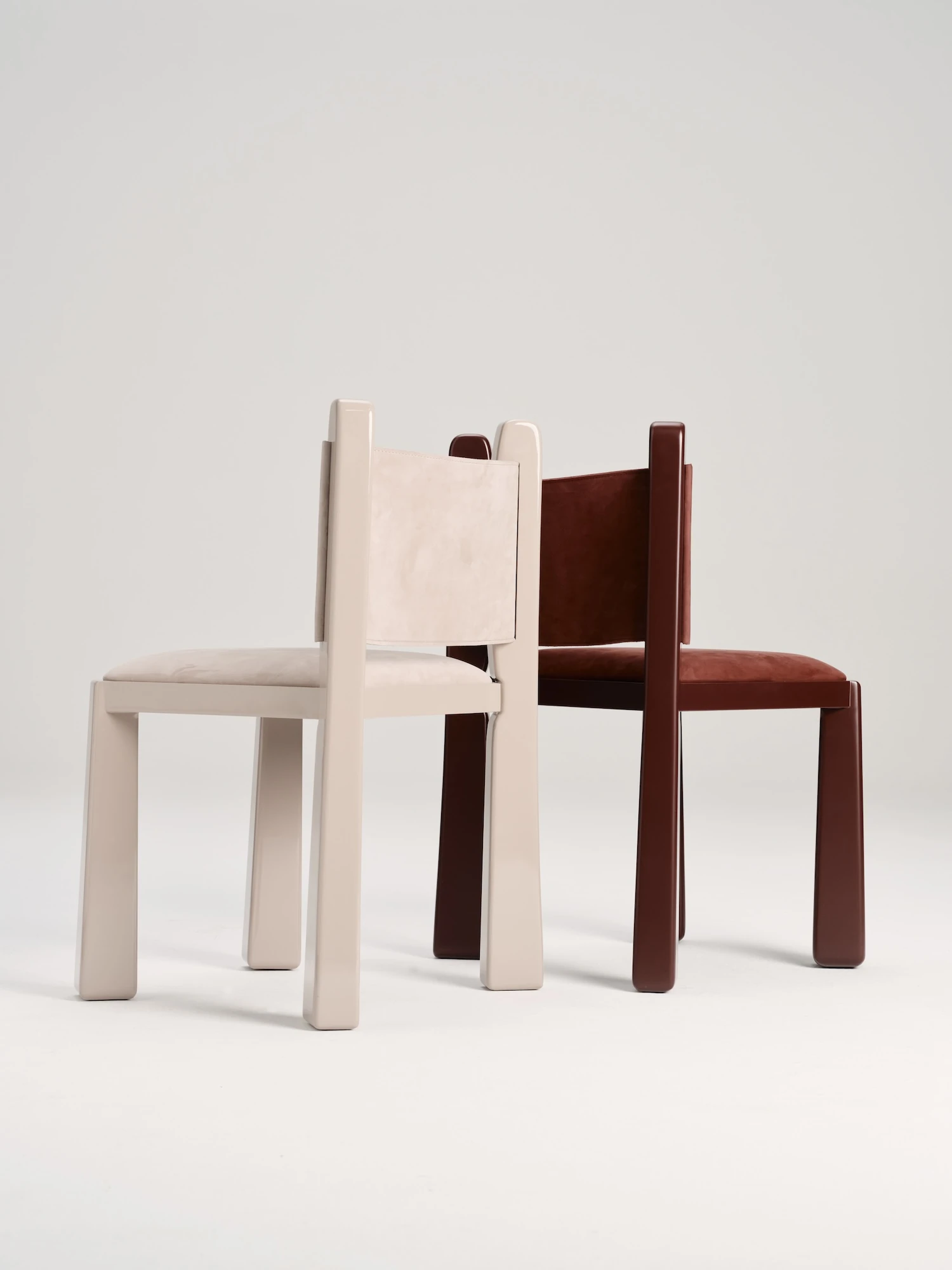 Ruby by NOVSEP, photographed by NOVSEP — A greige and an oxblood Ruby chair angled toward each other on a pale ground.