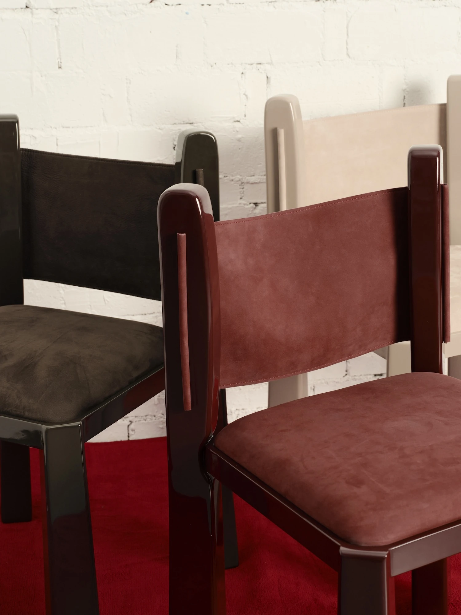 Ruby by NOVSEP, photographed by NOVSEP — Two Ruby chairs close together on a red floor, the oxblood suede back in the foreground and an espresso frame behind.