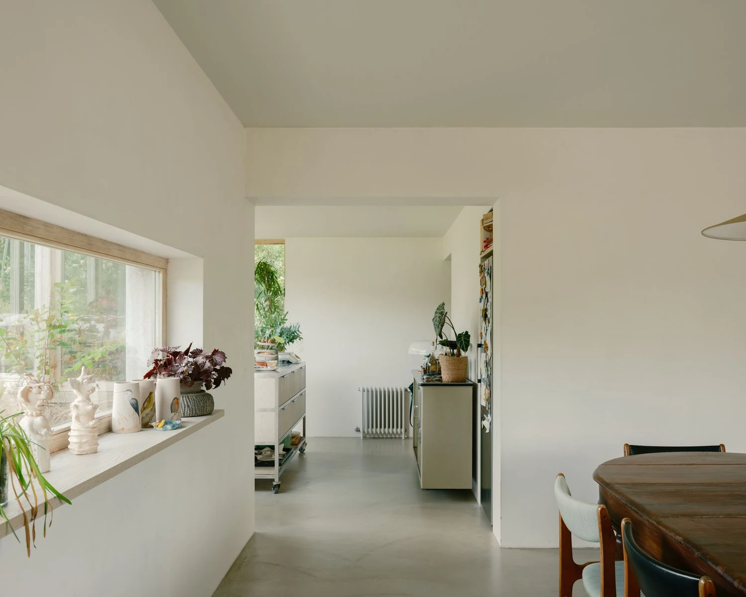 Casa de Souvinha by Parto Atelier, photographed by Francisco Ascensão, Parto Atelier — A deep window shelf holds a row of ceramics along a white plaster wall, the microcement floor running toward a dark antique table.
