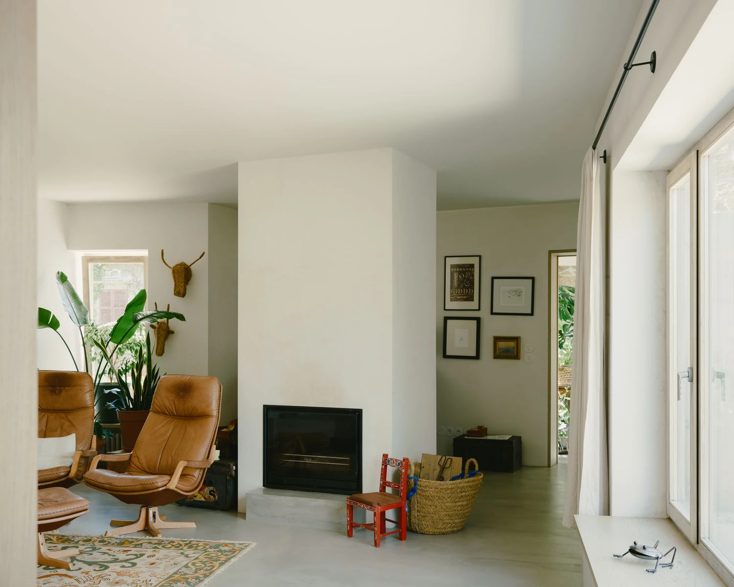 Casa de Souvinha by Parto Atelier, photographed by Francisco Ascensão, Parto Atelier — A plaster chimney breast holds a black steel fireplace at the heart of the living room, tan leather swivel chairs and a glazed garden door to either side.