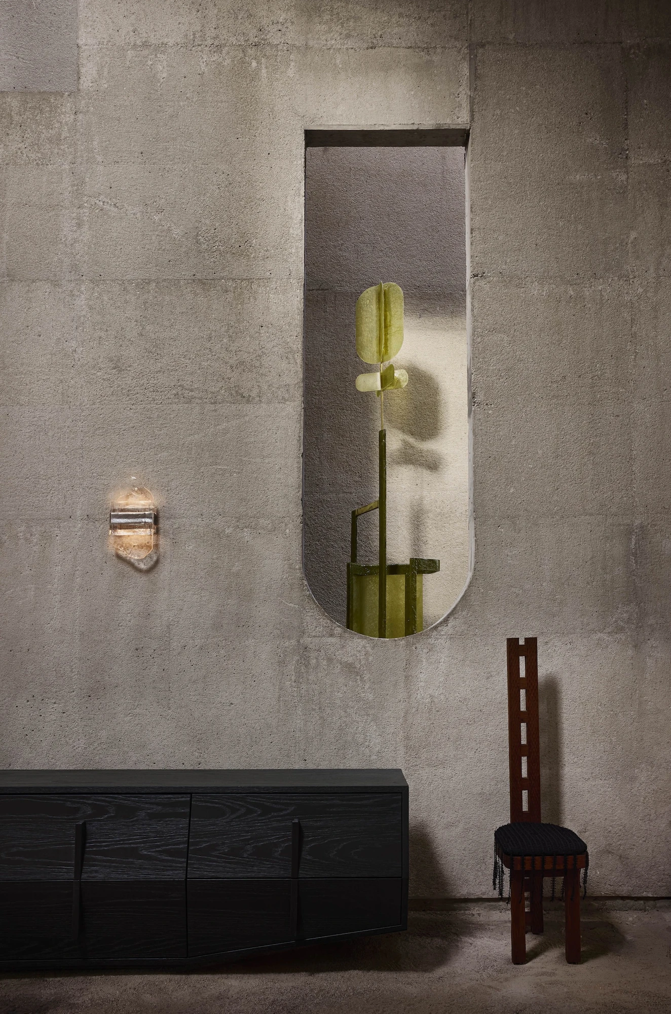 Casa Ínsula by TÁNAT, photographed by Alejandro Ramírez — A rock-crystal sconce and a tall arched niche holding an olive object rise above a black-oak sideboard, a red ladder-back chair set against the concrete.