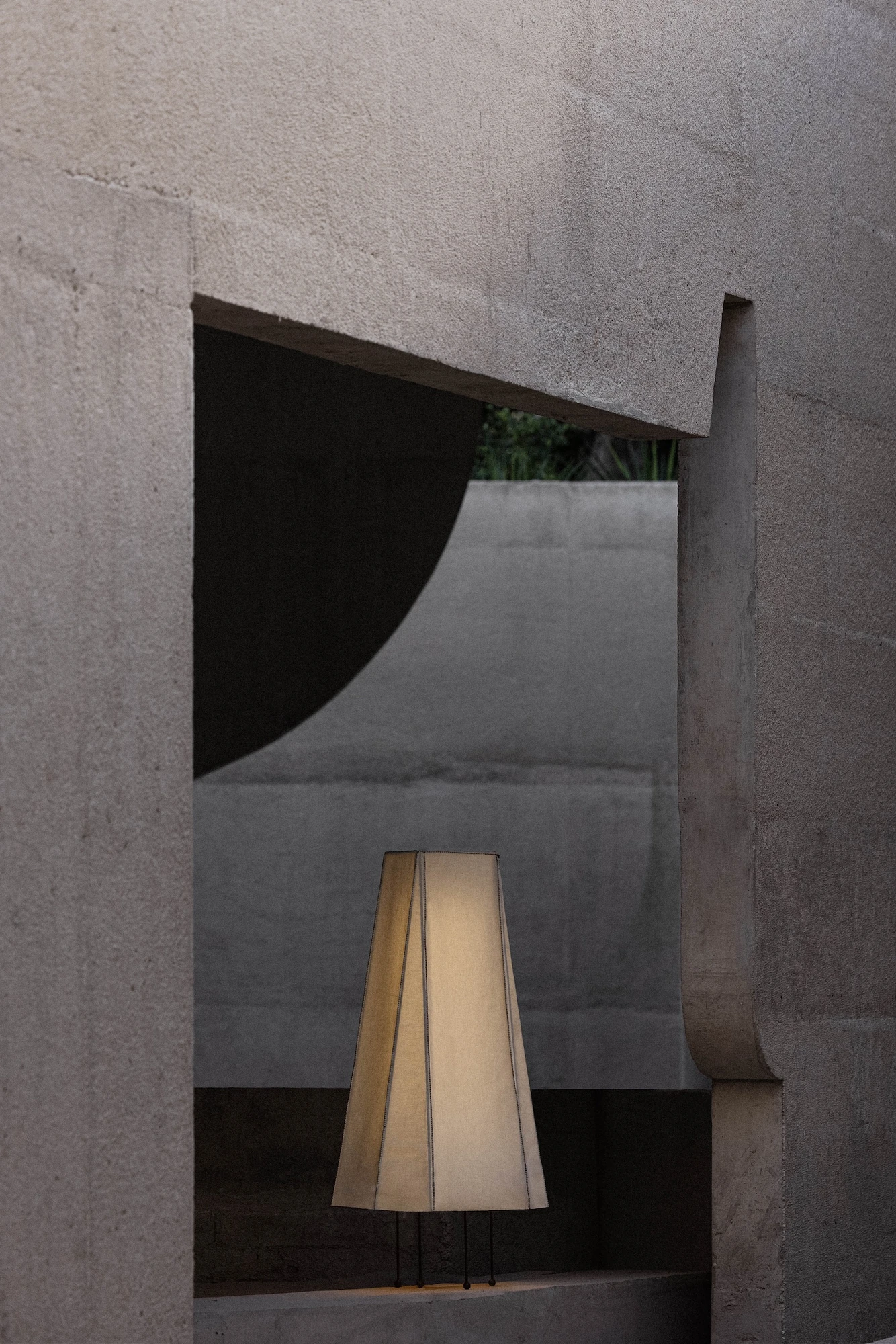 Casa Ínsula by TÁNAT, photographed by Alejandro Ramírez — A concrete doorway frames a conical fabric lamp, with a curved wall cut and a screen of daylight beyond.