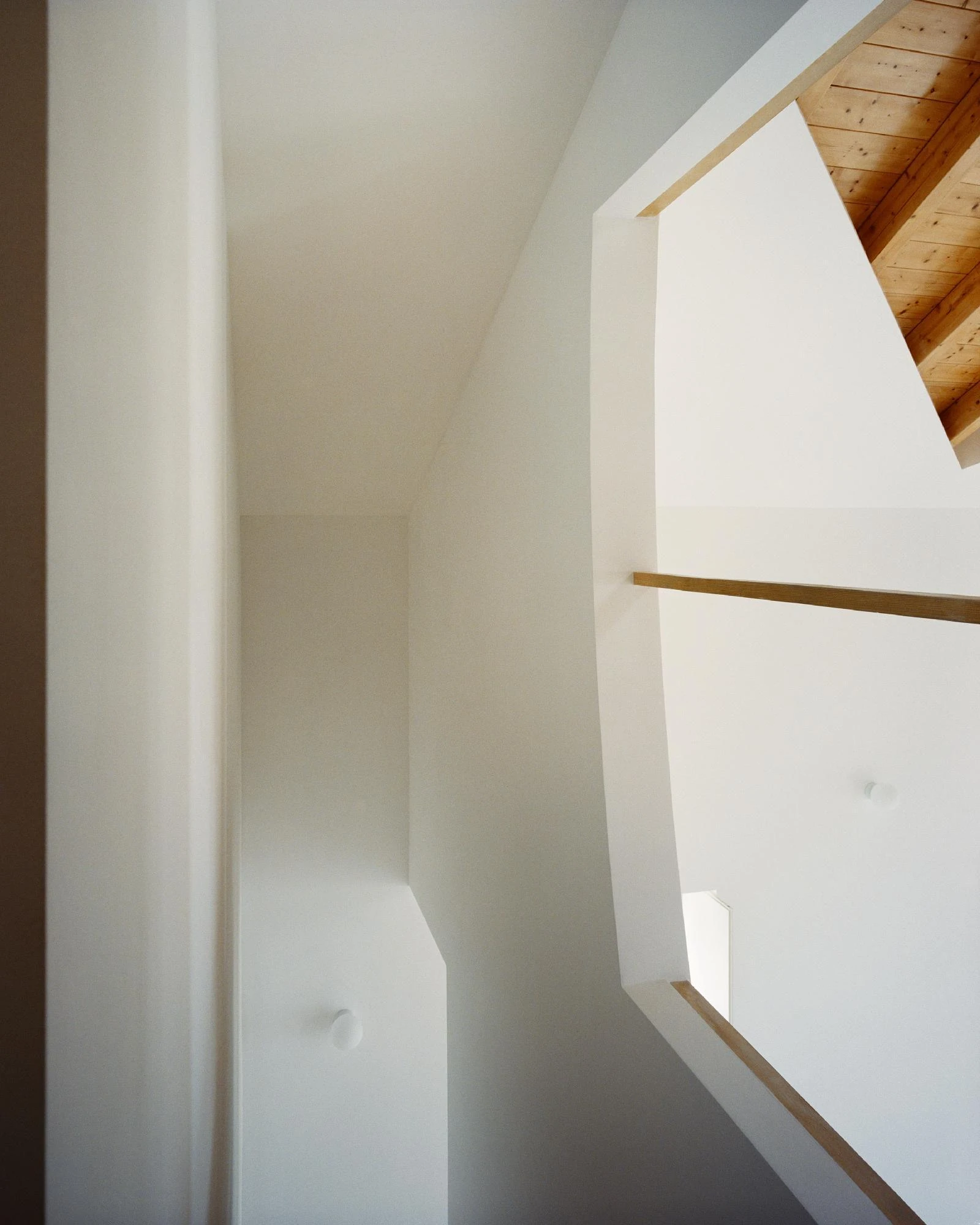 Cutouts by Corpo Atelier, photographed by Francisco Ascensão — An angular white void turns through faceted plaster planes, thin pine trim marking the edges as timber ceiling shows at the upper right.