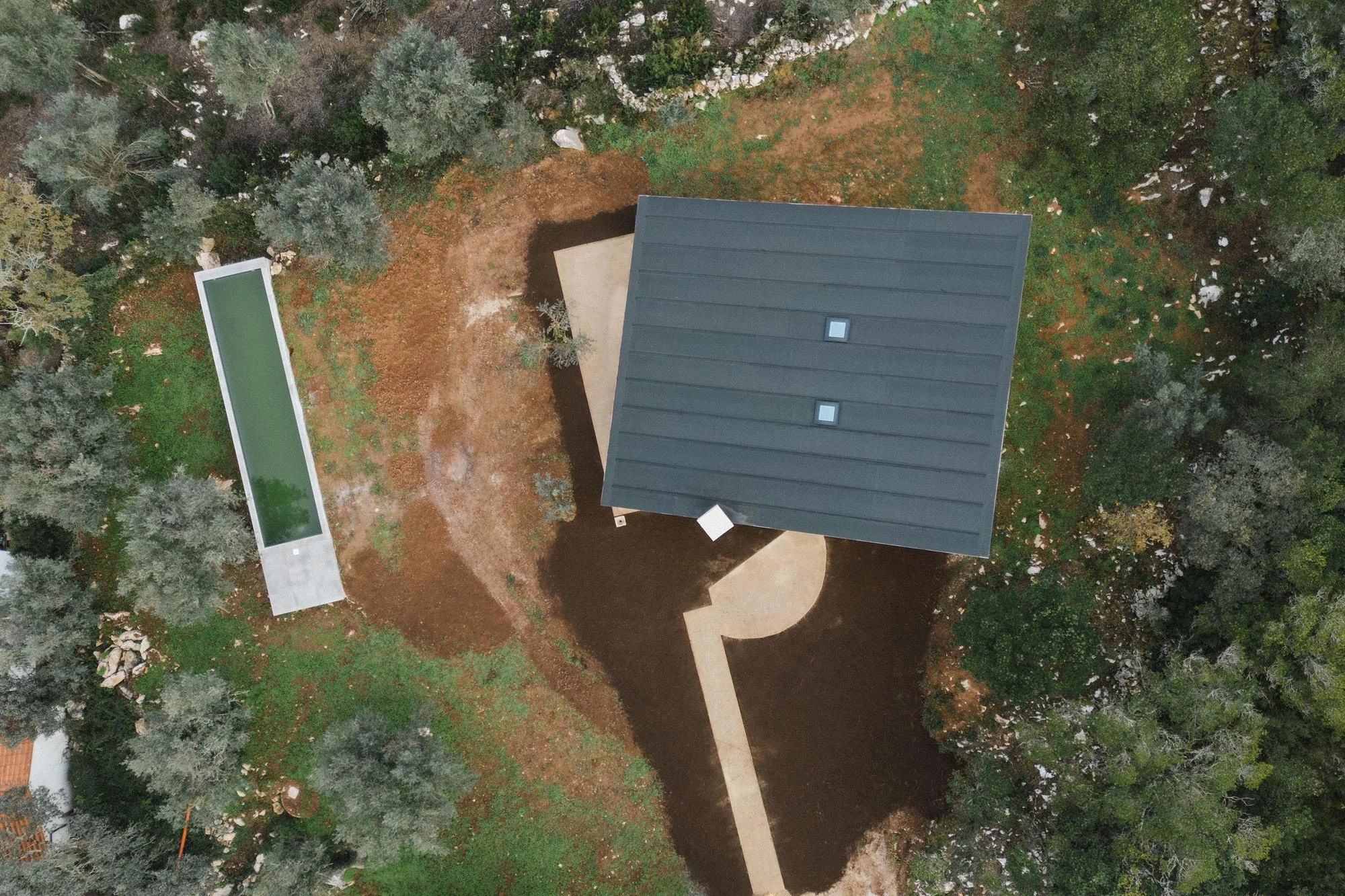 House in Cerrado by Atelier Espaço P2, photographed by José Campos — A top-down drone shot reads the dark rectangle of the roof, the slim green lap pool and the looping concrete path among olive trees.