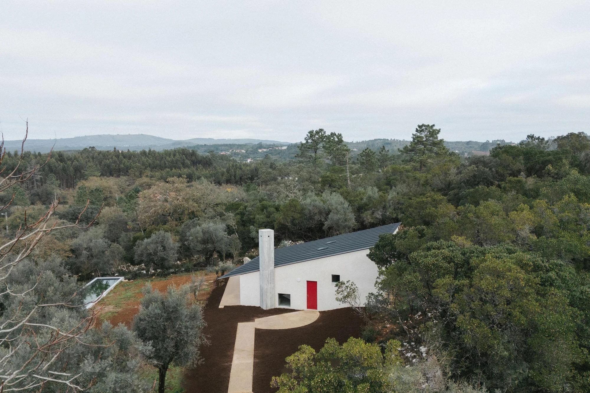 House in Cerrado by Atelier Espaço P2, photographed by José Campos — An aerial view sets the dark-roofed house and its long lap pool against dense woodland and distant blue hills.