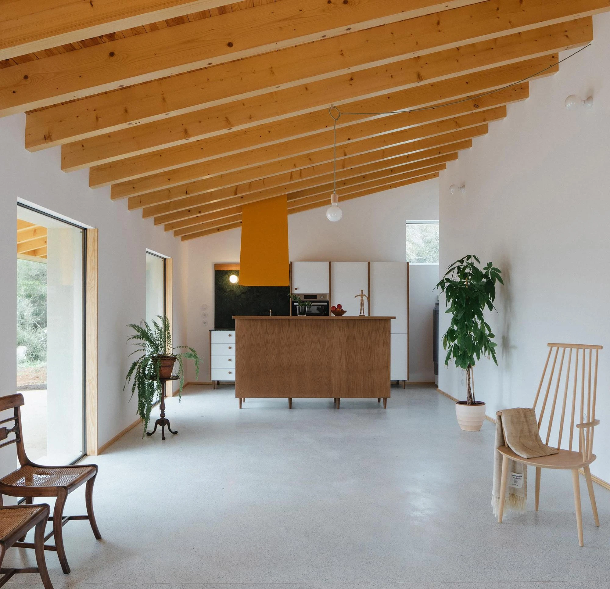 House in Cerrado by Atelier Espaço P2, photographed by José Campos — The open main room runs beneath exposed pine beams and a boarded ceiling, an oak island and ochre-yellow hood set on a pale terrazzo floor.