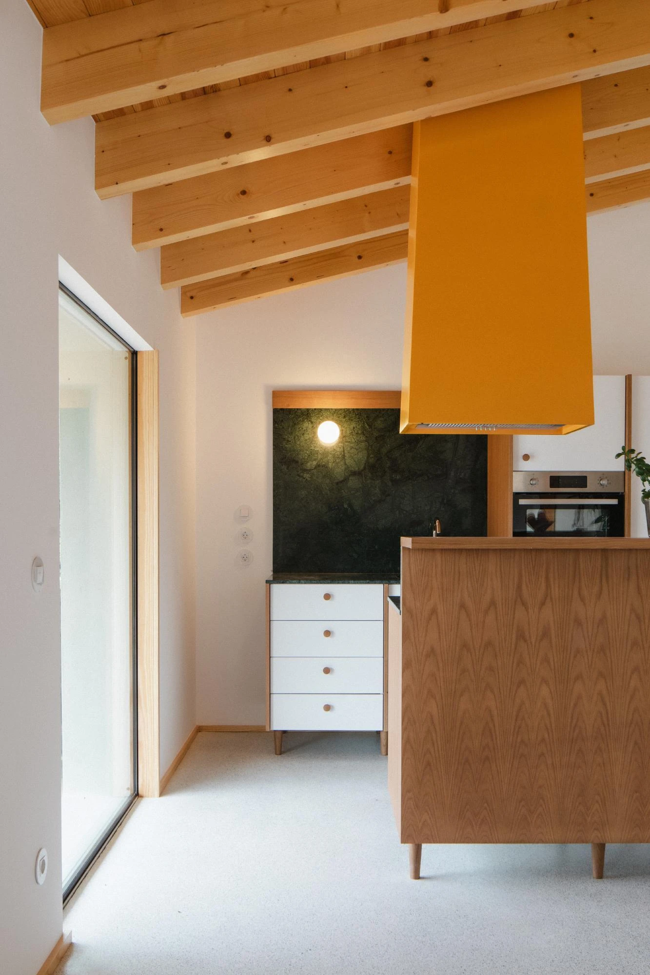 House in Cerrado by Atelier Espaço P2, photographed by José Campos — A kitchen detail pairs the ochre-yellow extractor hood with a green marble backsplash and white-and-wood drawers under pine beams.