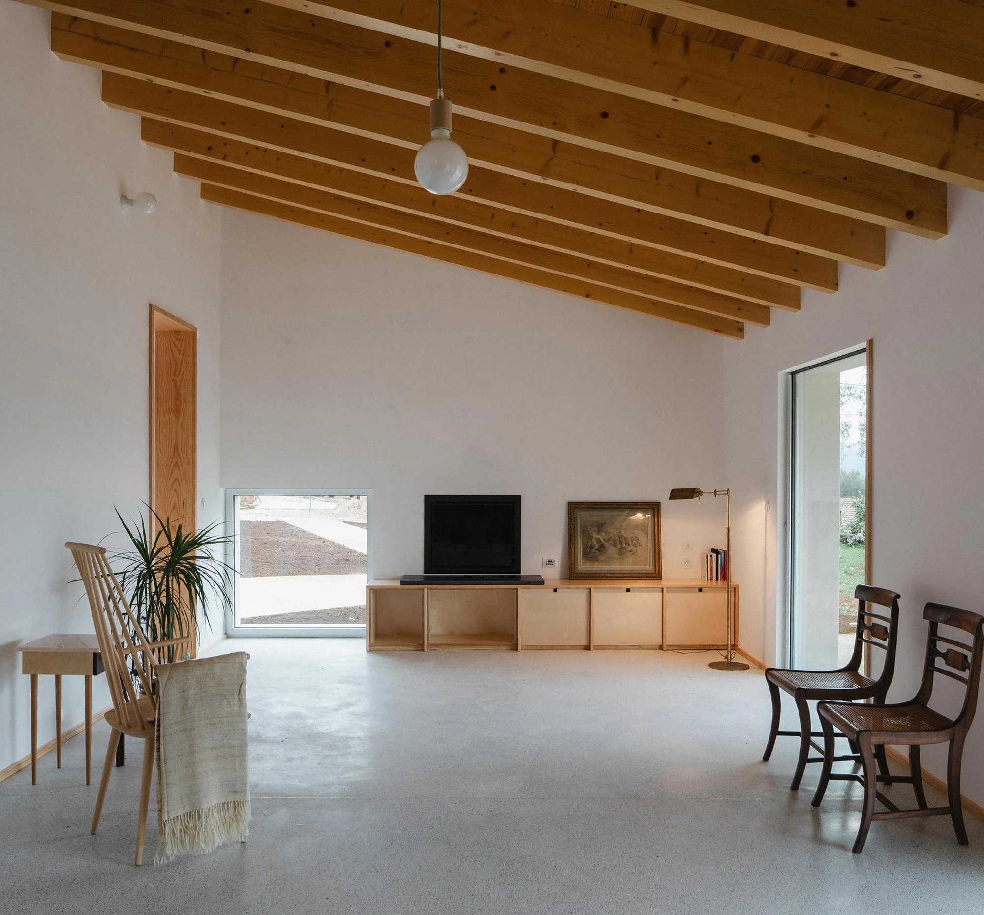 House in Cerrado by Atelier Espaço P2, photographed by José Campos — The living area sets a birch plywood media unit and mid-century wooden chairs against white walls and a pale terrazzo floor.