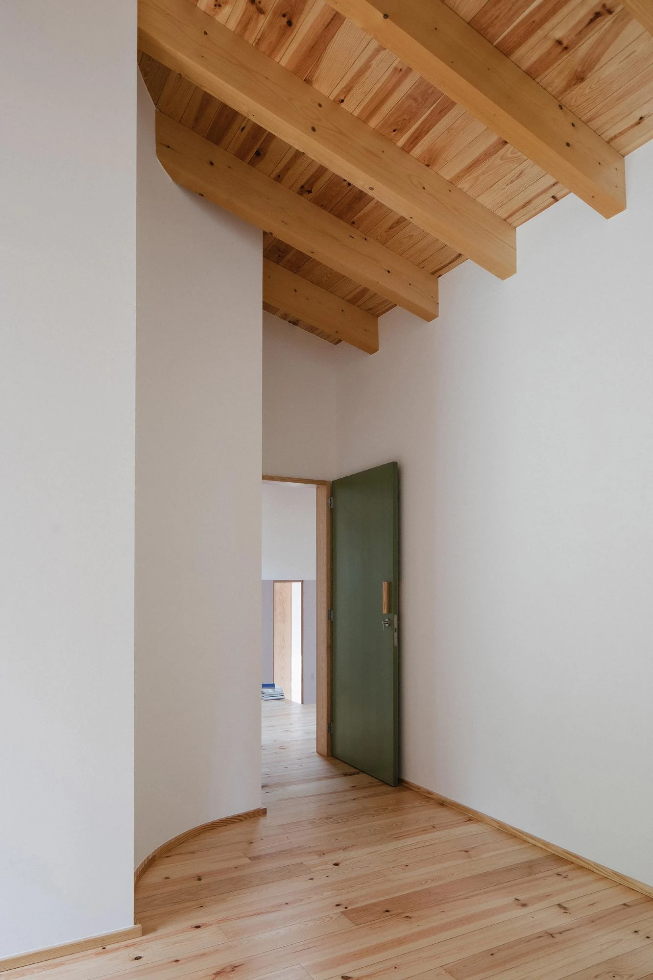House in Cerrado by Atelier Espaço P2, photographed by José Campos — A tall white hallway rises to a pine-boarded ceiling, a forest-green door in a pale timber frame opening onto a pine plank floor.