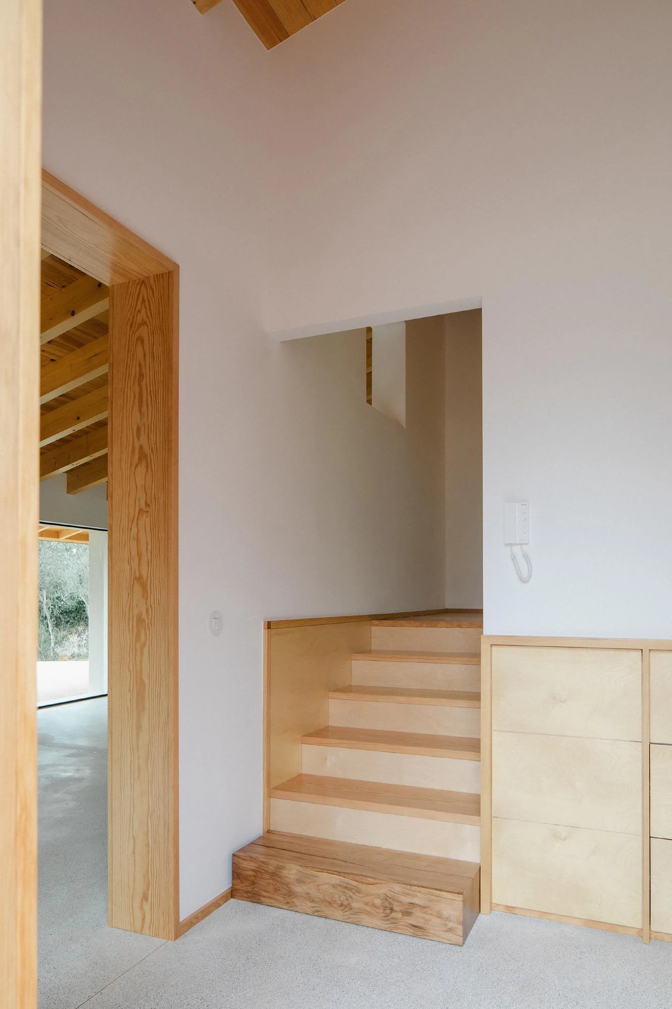 House in Cerrado by Atelier Espaço P2, photographed by José Campos — A short flight of birch plywood stairs meets a built-in cabinet beside a pine door frame on a terrazzo floor.