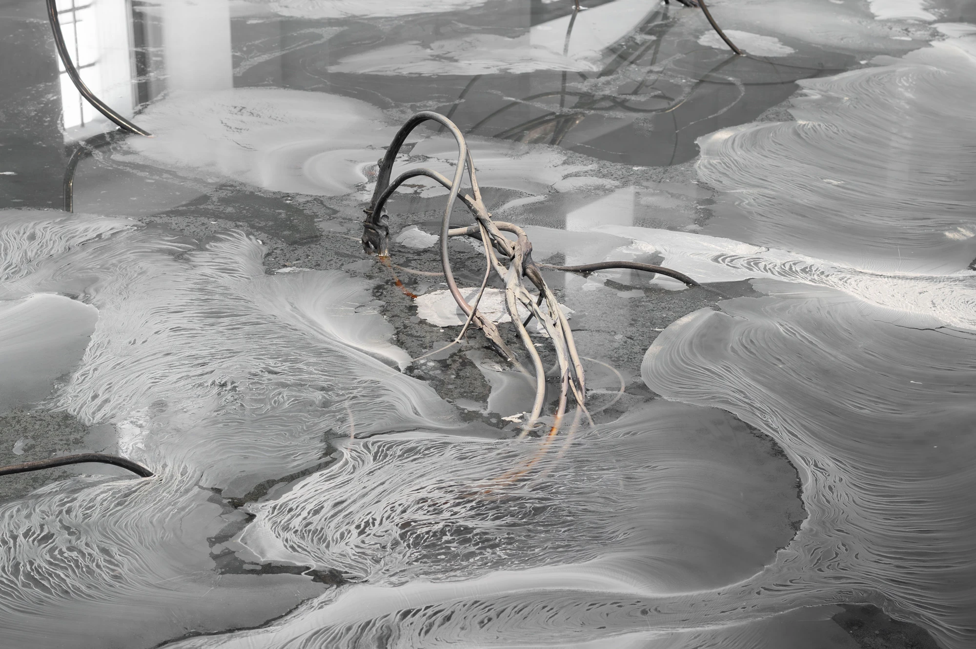 Accomplice by Yein Lee, photographed by Blaž Gutman / MGML — Detail of the ground-based pool, cables dipping into a surface streaked with pale swirled sediment.