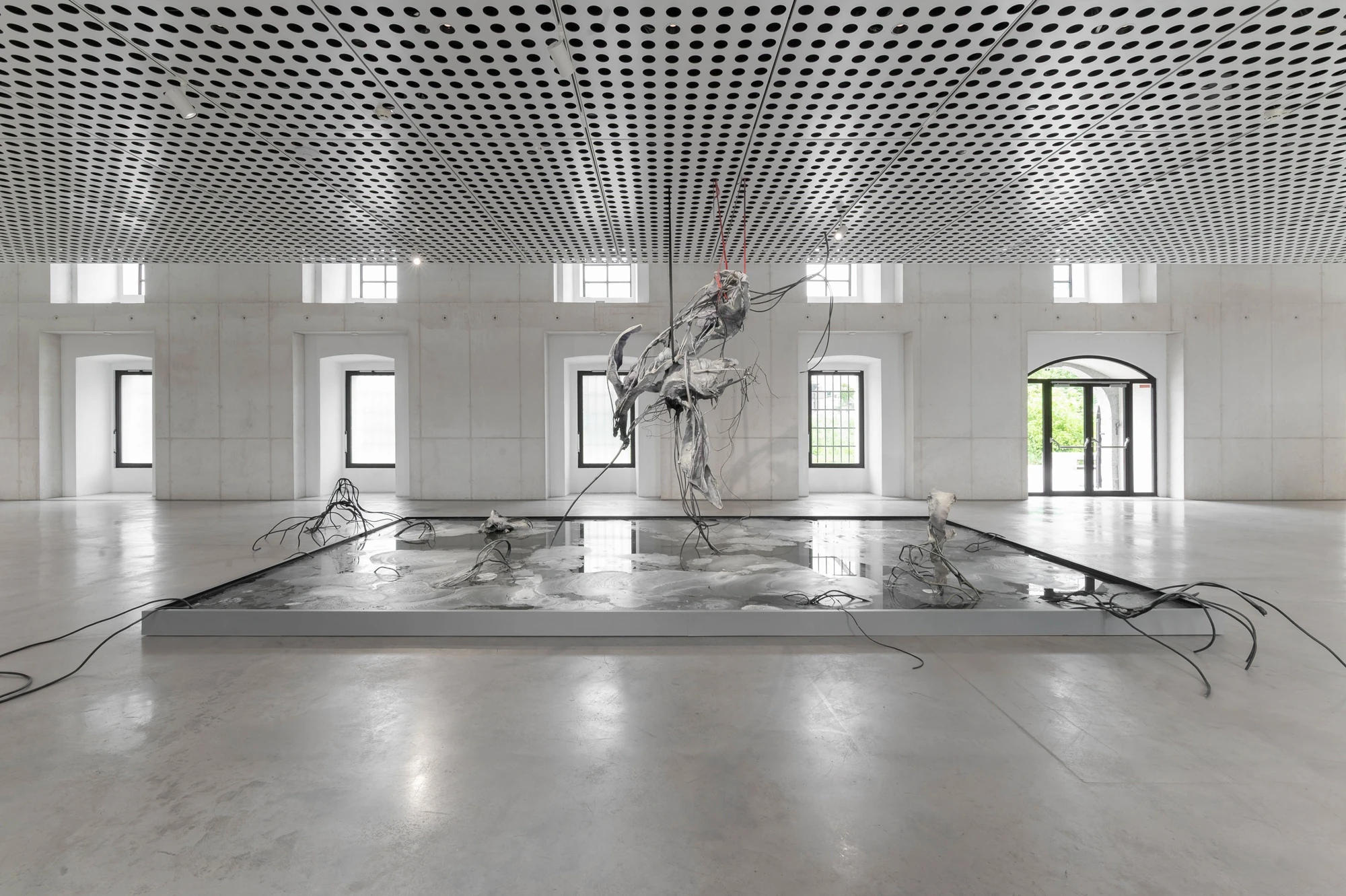 Accomplice by Yein Lee, photographed by Blaž Gutman / MGML — Wide view of the central suspended sculpture reaching over the pool, cabling spilling across the concrete floor.