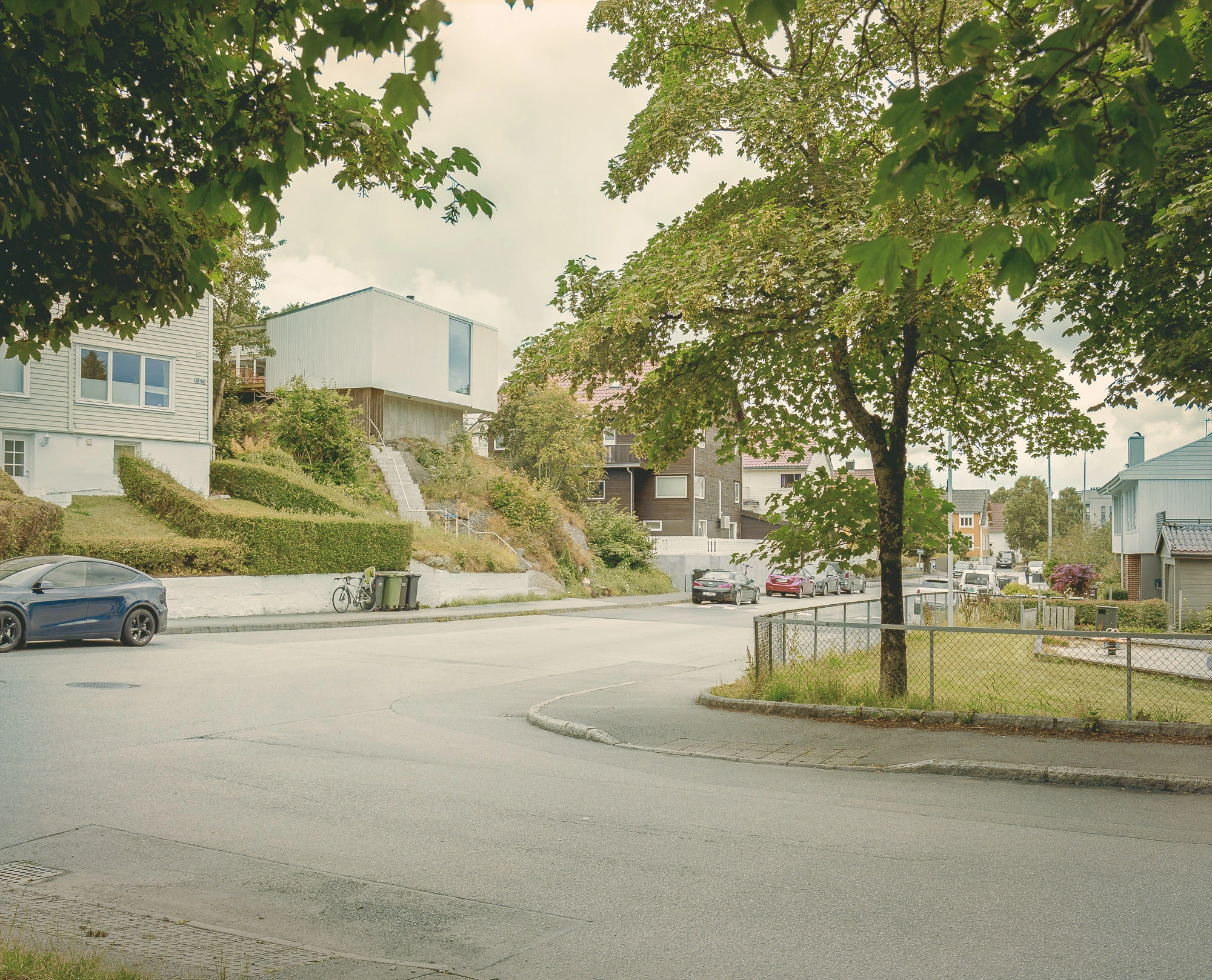 Ersland & Skeie House by Knut Hjeltnes Architects, photographed by Hugo Lütcherath — The white house rises above a steep bedrock slope among the older timber houses of a semi-dense Stavanger neighbourhood.