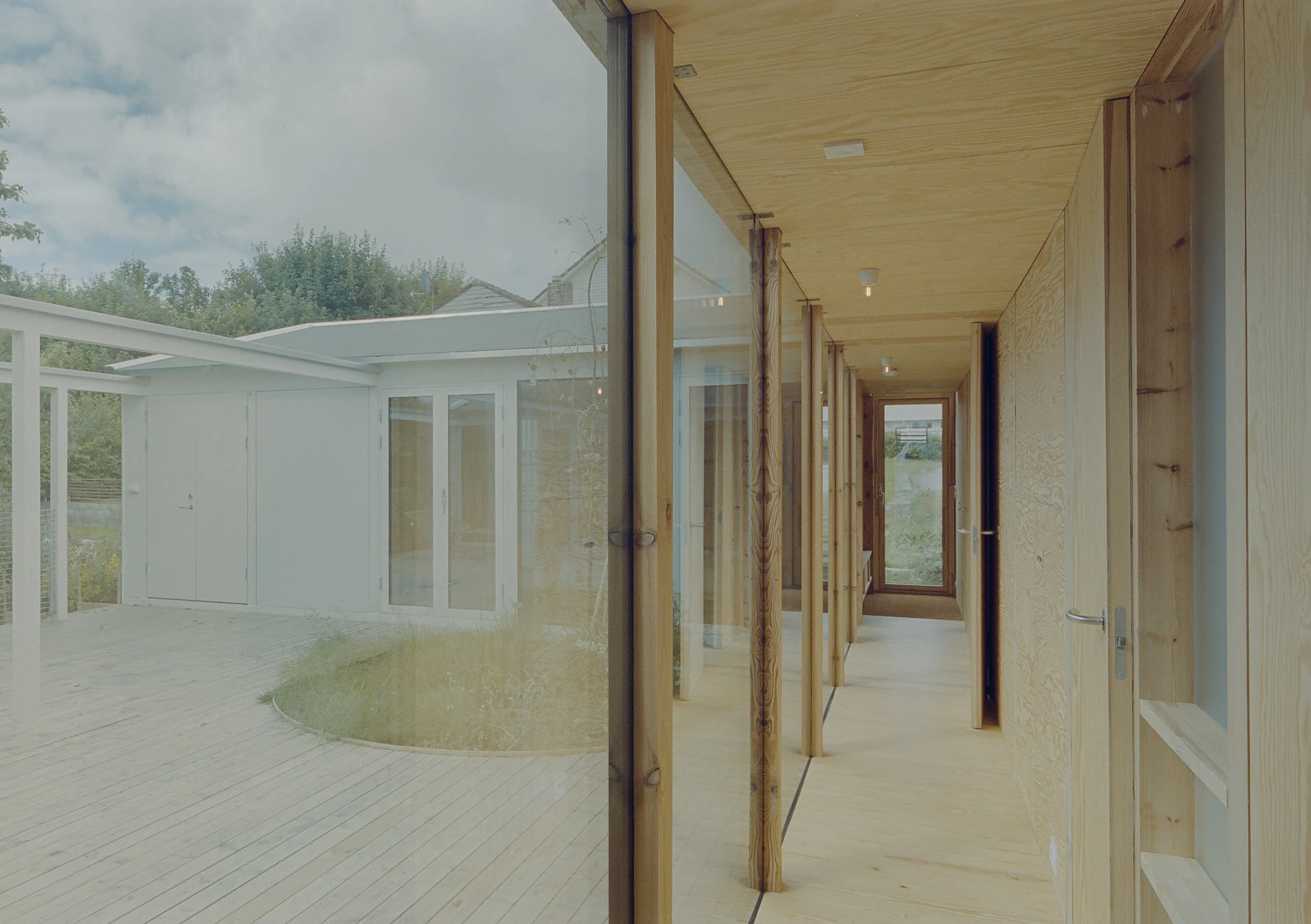 Ersland & Skeie House by Knut Hjeltnes Architects, photographed by Hugo Lütcherath — A glazed gallery runs behind visible pine posts and beams, the piazzetta on one side and rooms on the other.