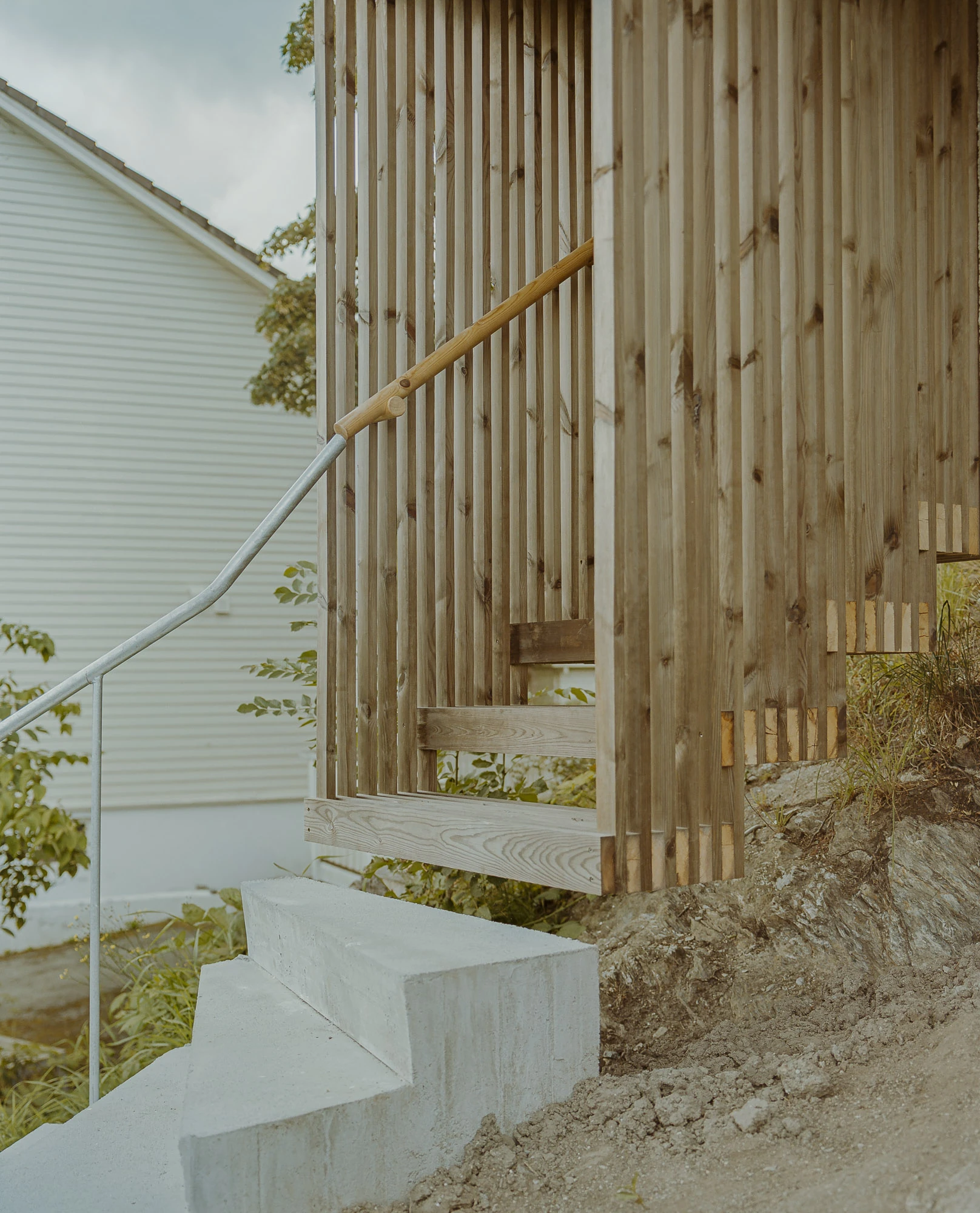 Ersland & Skeie House by Knut Hjeltnes Architects, photographed by Hugo Lütcherath — A detail of the hanging entry stair, timber slats and a concrete step set directly against the exposed rock.