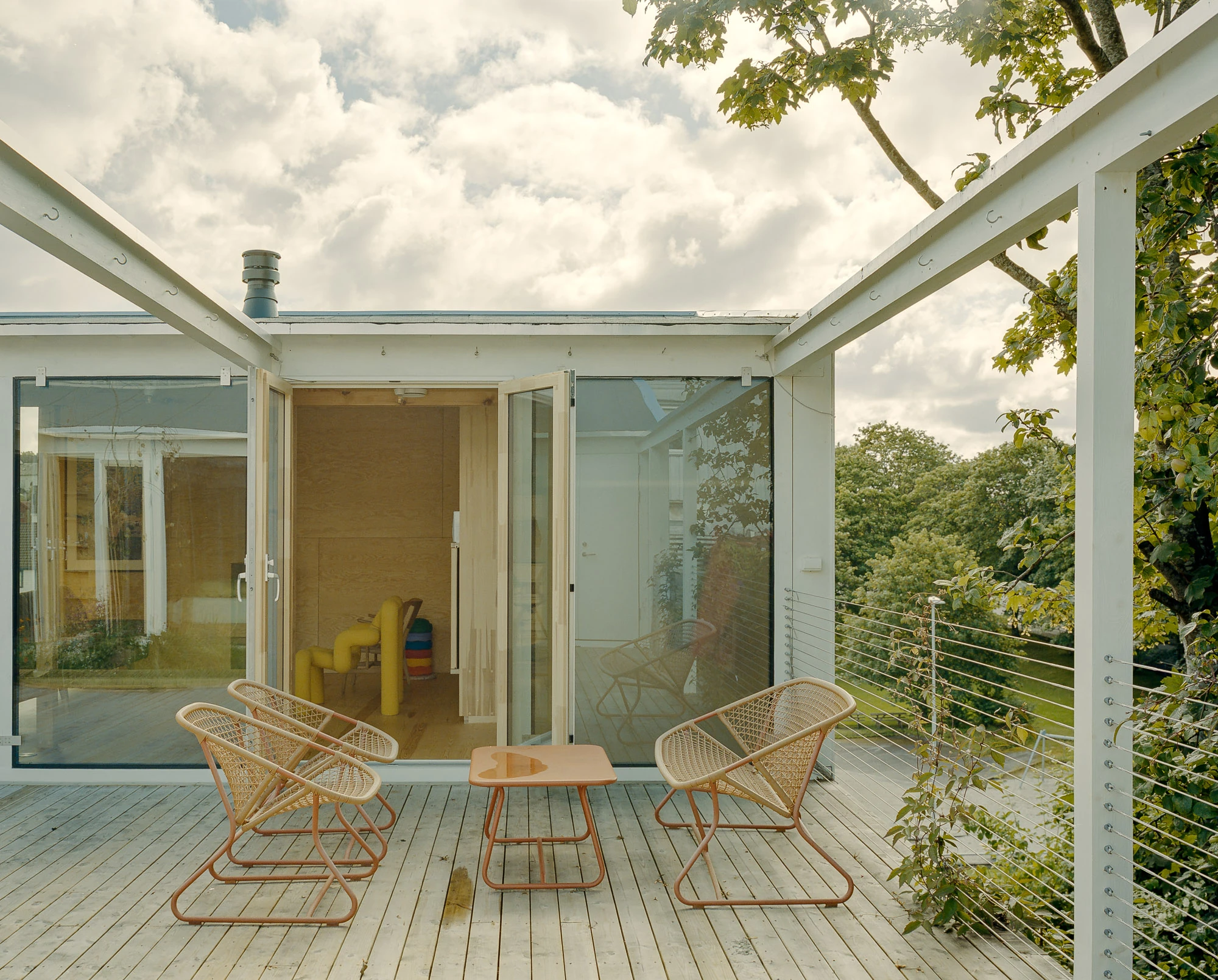 Ersland & Skeie House by Knut Hjeltnes Architects, photographed by Hugo Lütcherath — A woven rope bench sits against the glass, framing the planted piazzetta beyond.