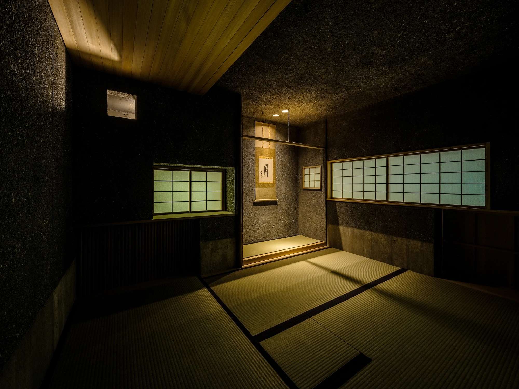 Konkuri-an by Teitakusubako, Yusuke Igarashi Architects, photographed by Kentaro Nemoto, Kazumasa Harada — The tea room after dark, paper screens glowing over the concrete walls, an alcove lit at the room's end.