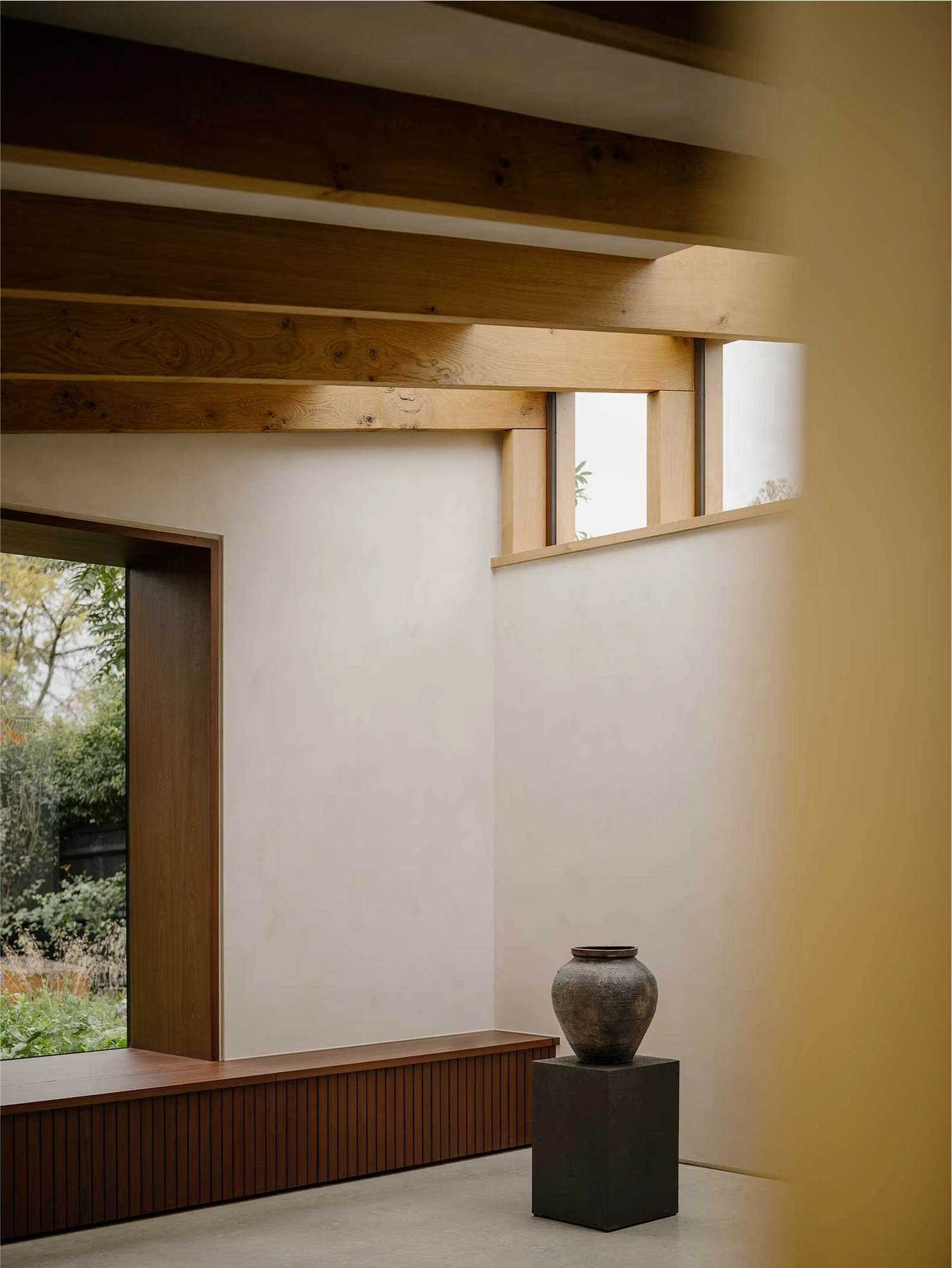 Muttram Veedu by Will Gamble Architects, photographed by James Retief — Exposed oak joists cross the living space above a low bench, a tall reveal framing the garden.