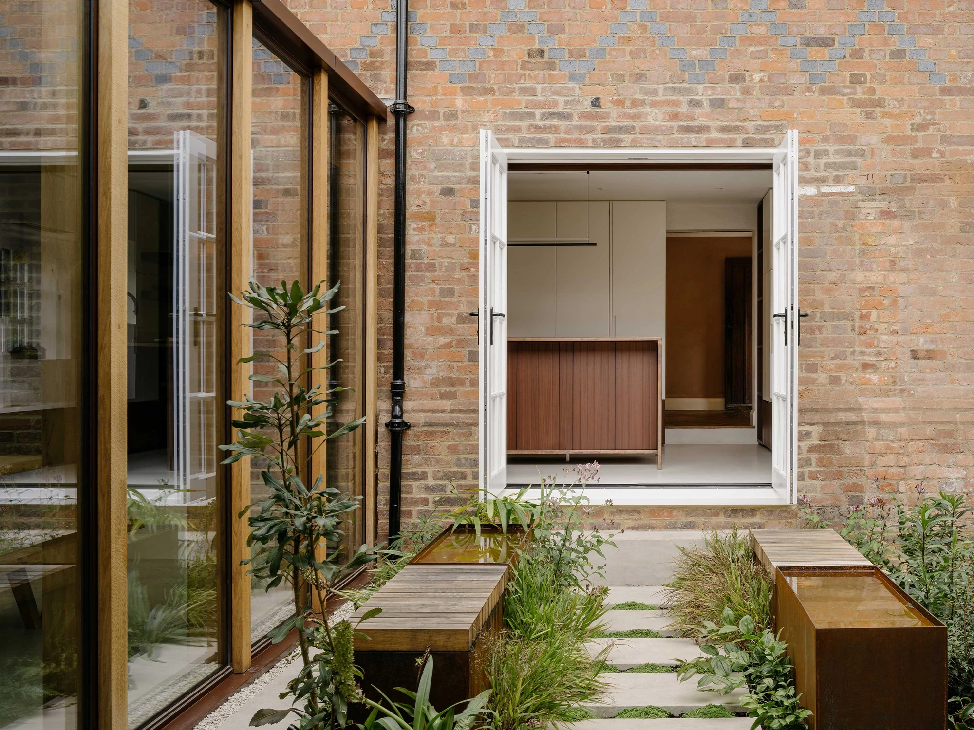 Muttram Veedu by Will Gamble Architects, photographed by James Retief — Oak joists meet a high clerestory slot above a plastered wall, an earthenware jar on a plinth below.