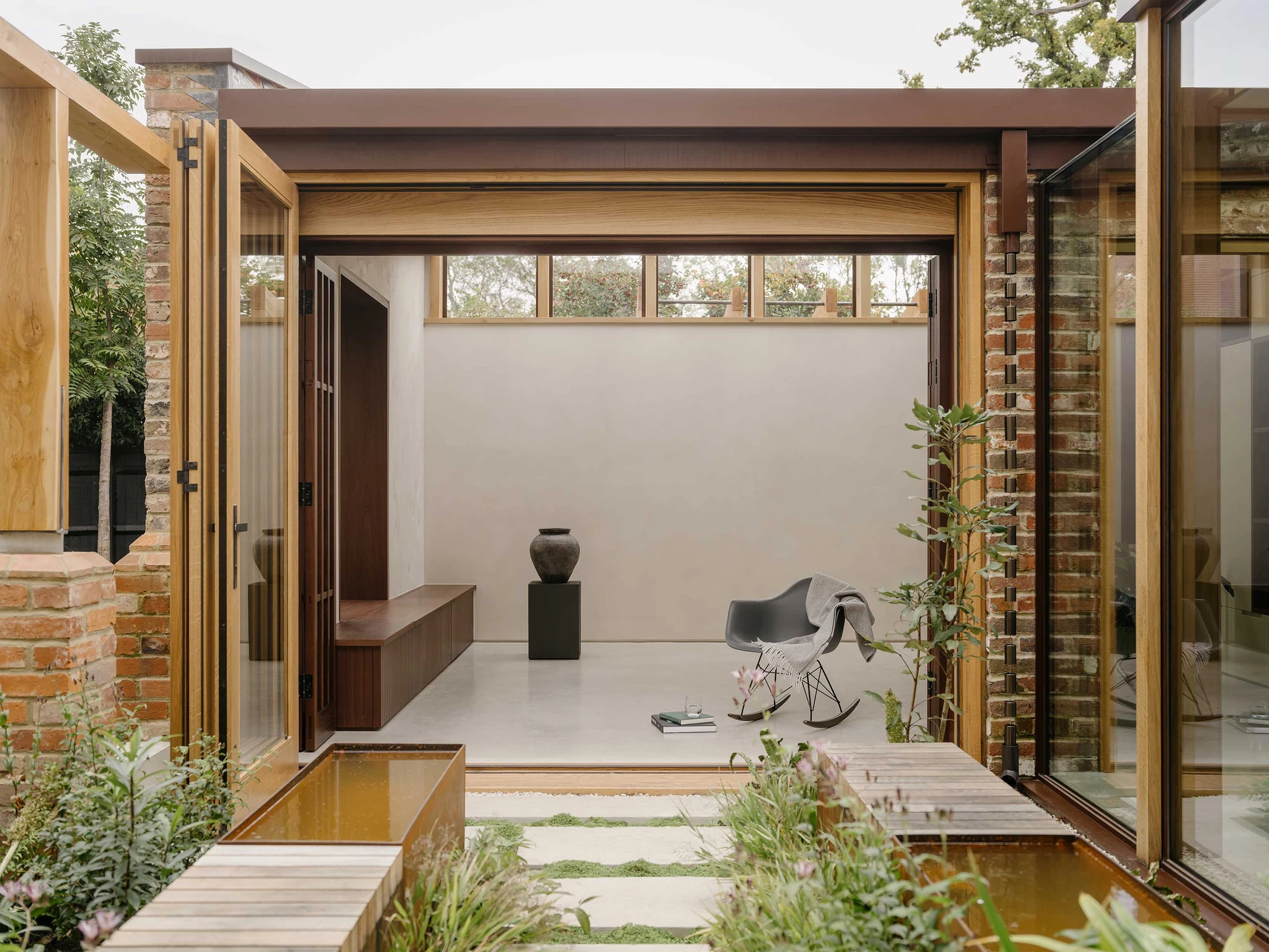 Muttram Veedu by Will Gamble Architects, photographed by James Retief — Sapele bifolding shutters and the glazed link meet at the courtyard, a timber walkway crossing the water.