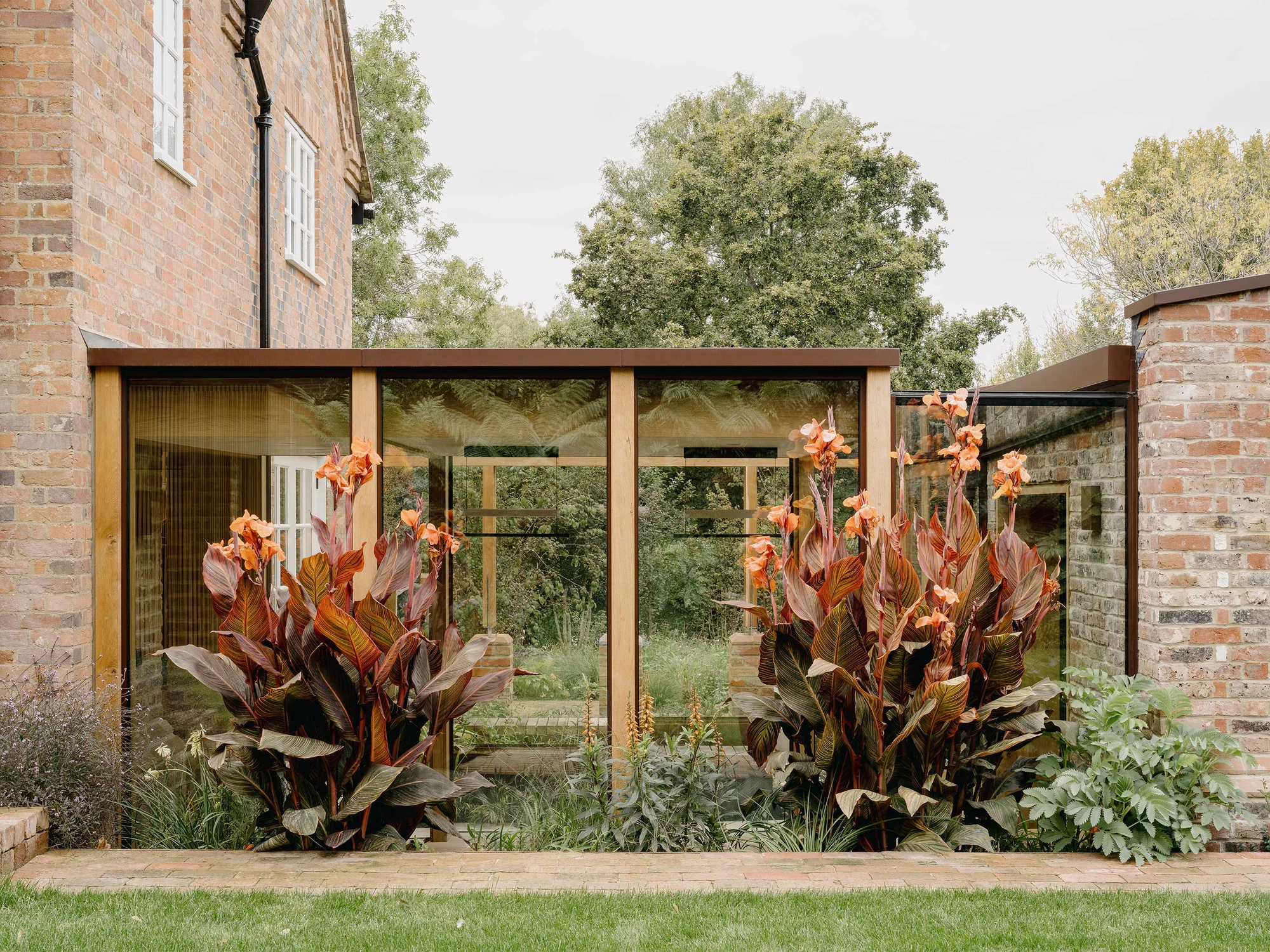 Muttram Veedu by Will Gamble Architects, photographed by James Retief — The cottage gable and the new brick wall enclose the glazed courtyard link, planting massed at its base.